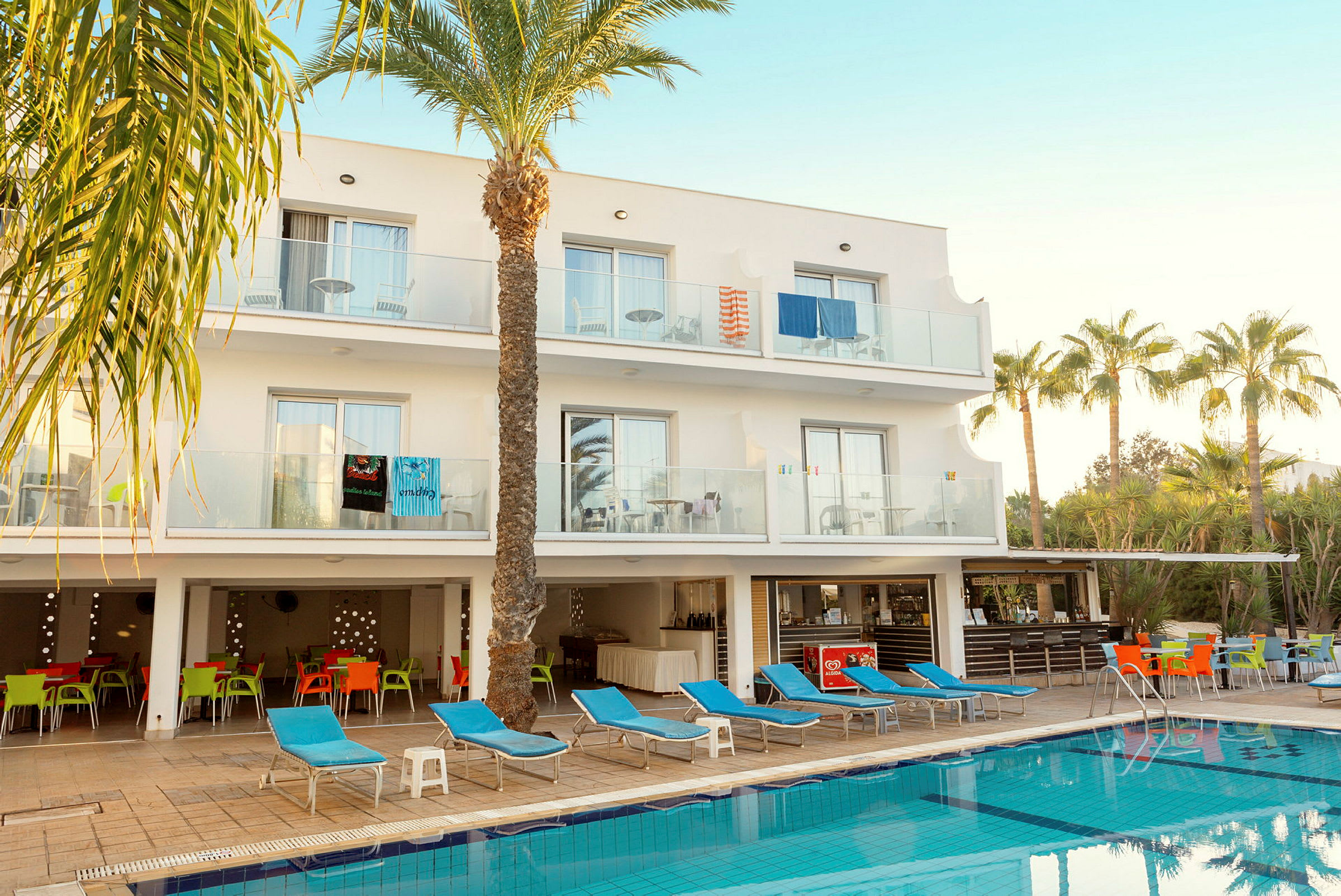 Hotell med balkonger, solstolar och pool i förgrunden. (AI-genererad text)