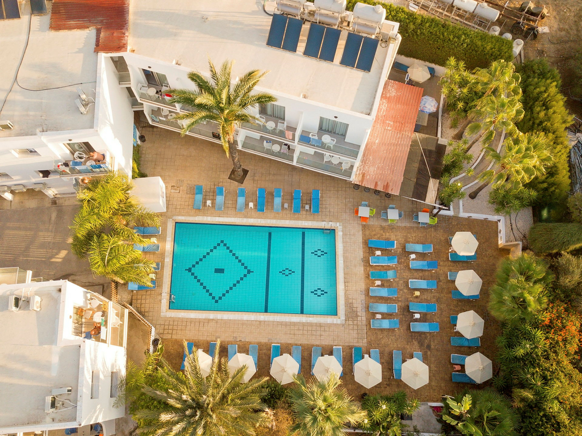 Flygbild av hotellpool med solstolar och parasoller omkring. (AI-genererad text)