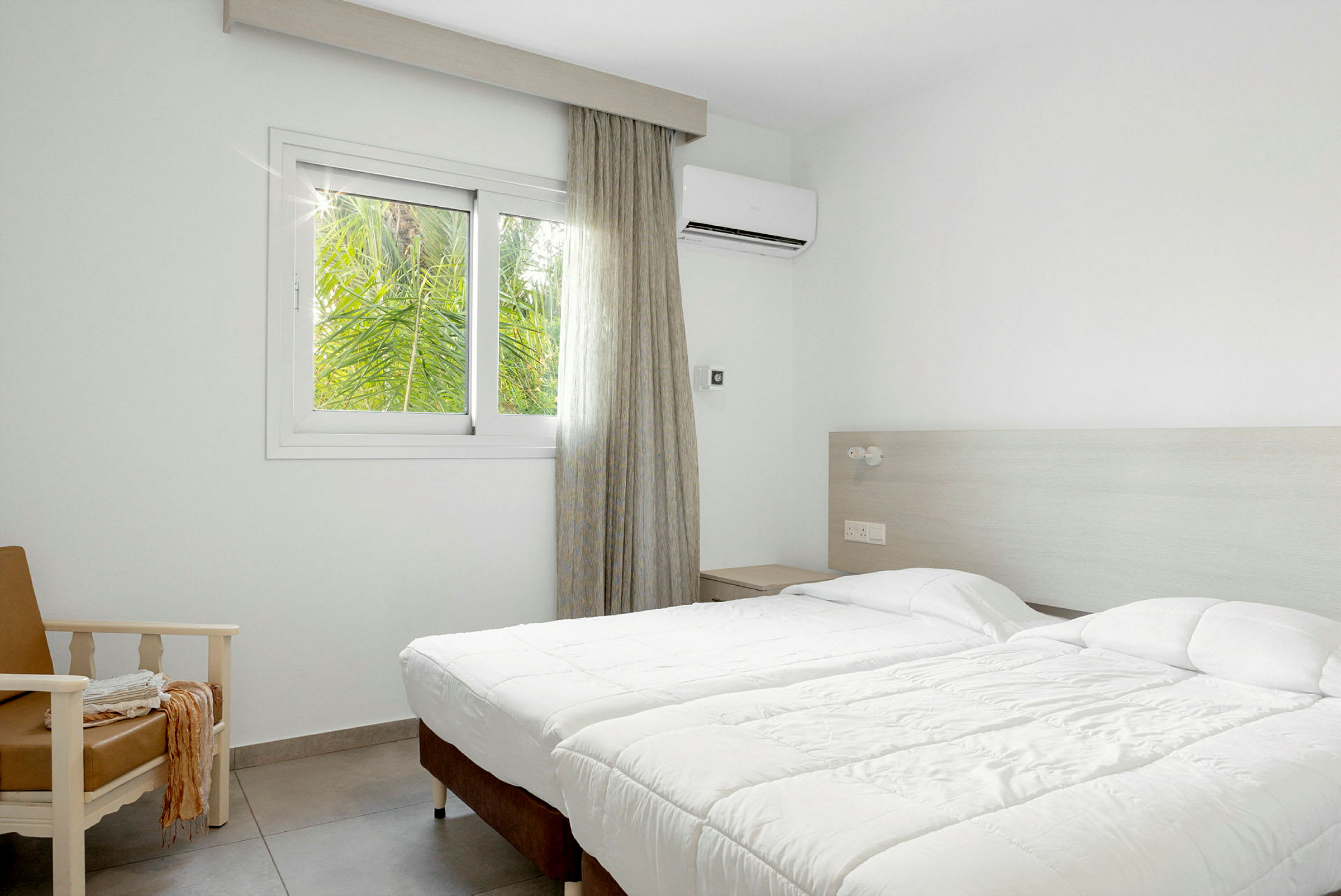 Hotellrum med två enkelsängar, en fåtölj och ett fönster med utsikt mot grönska. (AI-genererad text)