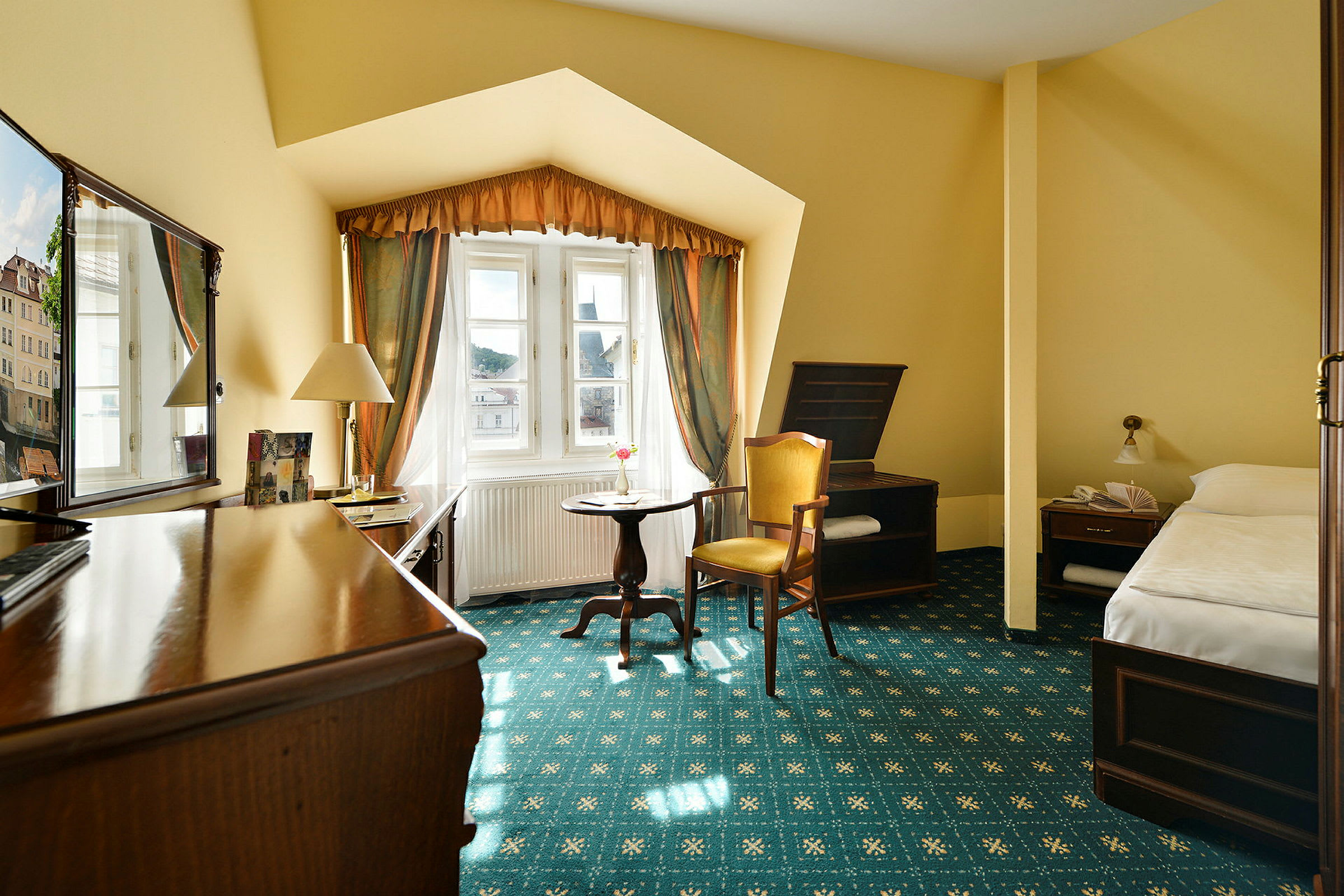 Ett hotellrum med gult tema, inkluderande säng, fåtölj, skrivbord och ett fönster med gardiner. (AI-genererad text)