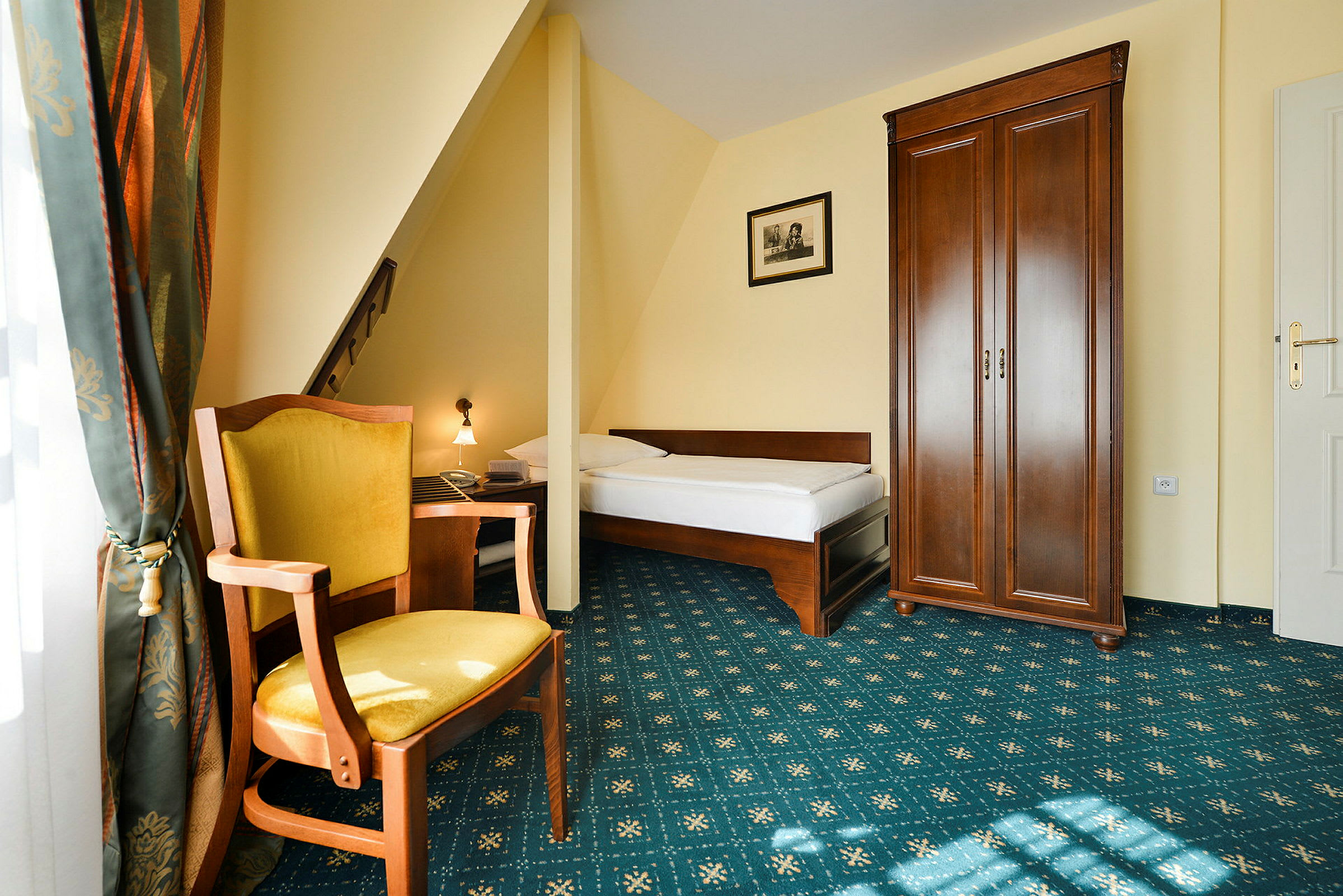 Ett hotellrum med en enkelsäng, en trästol med gul sits, ett högt klädskåp och ett fönster med gardiner. (AI-genererad text)