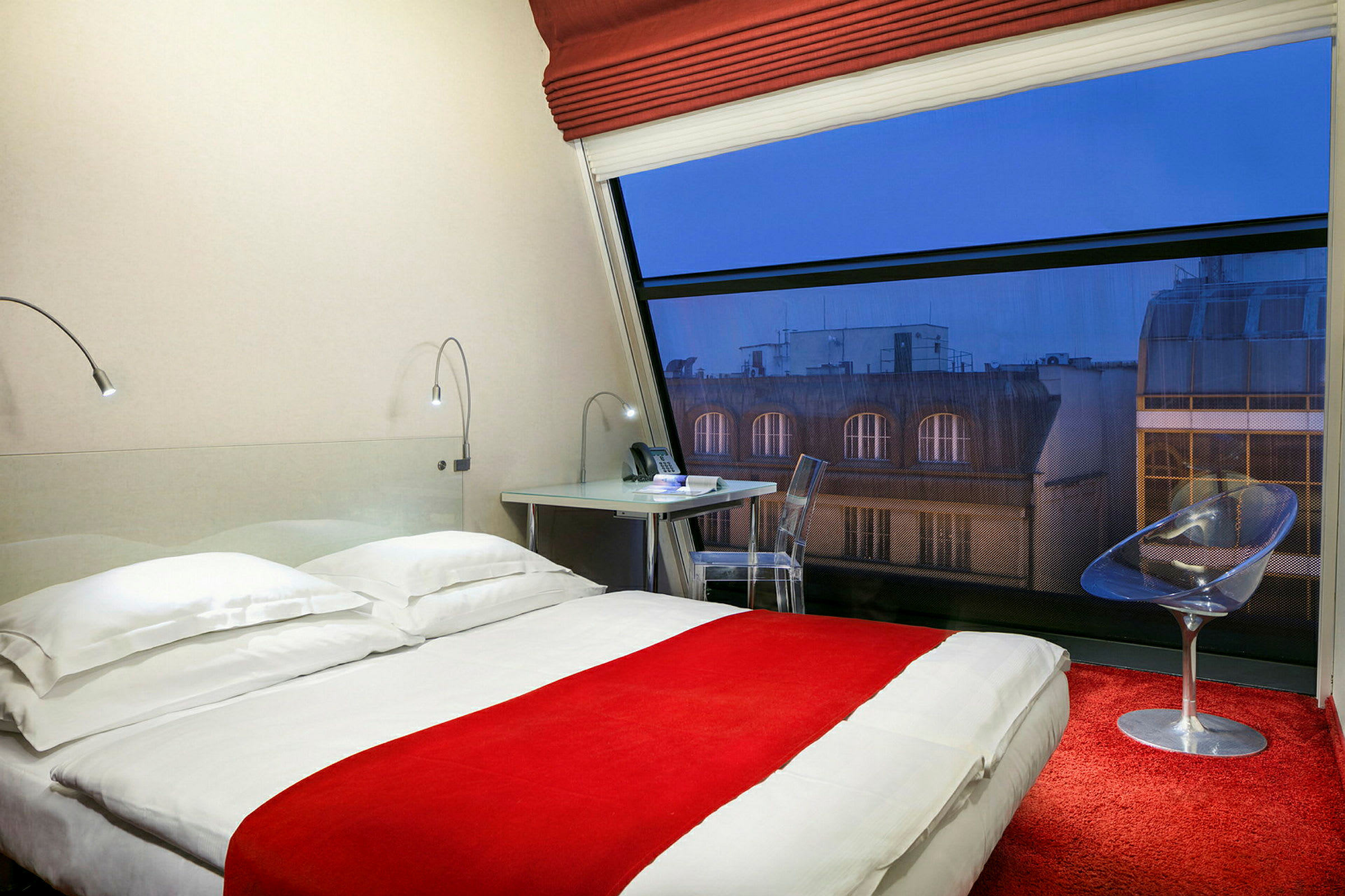 Hotellrum med en säng, skrivbord och stol samt ett stort fönster med utsikt. (AI-genererad text)