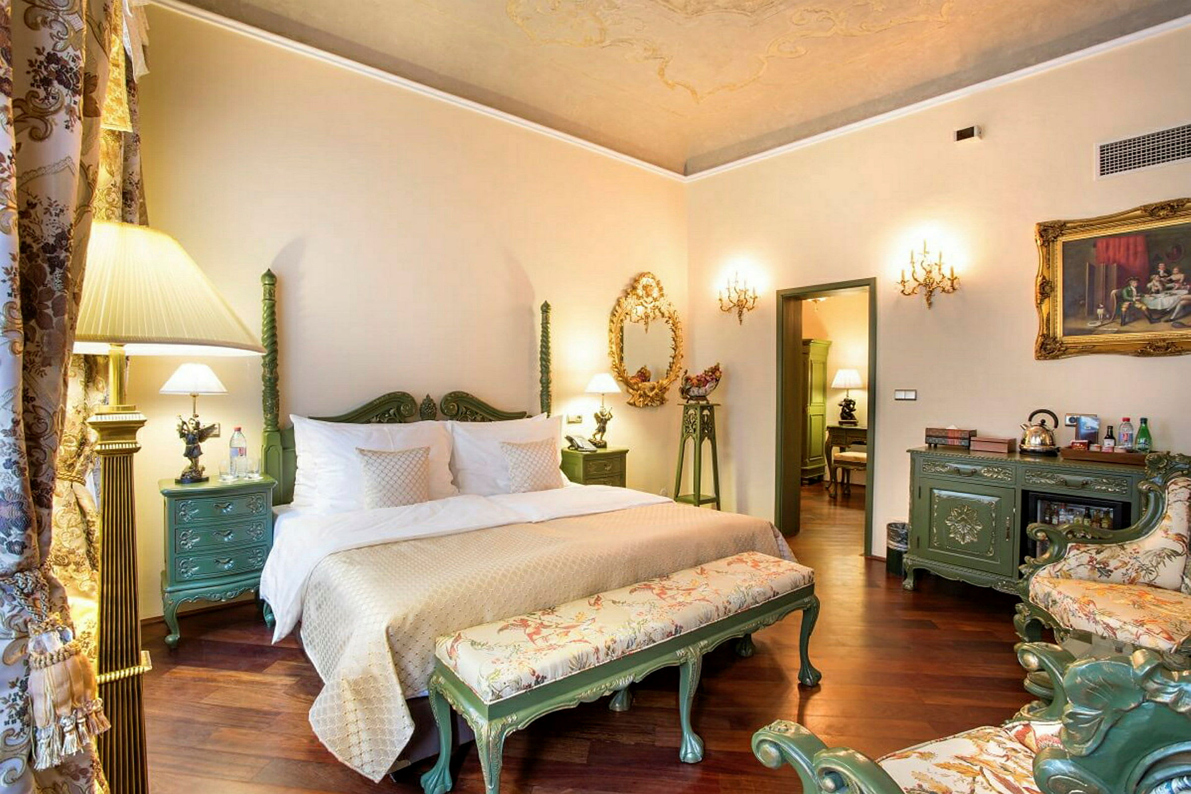 Ett hotellrum med en stor dubbelsäng och elegant inredning i traditionell stil, inklusive gröna möbler och dekorativa detaljer. (AI-genererad text)
