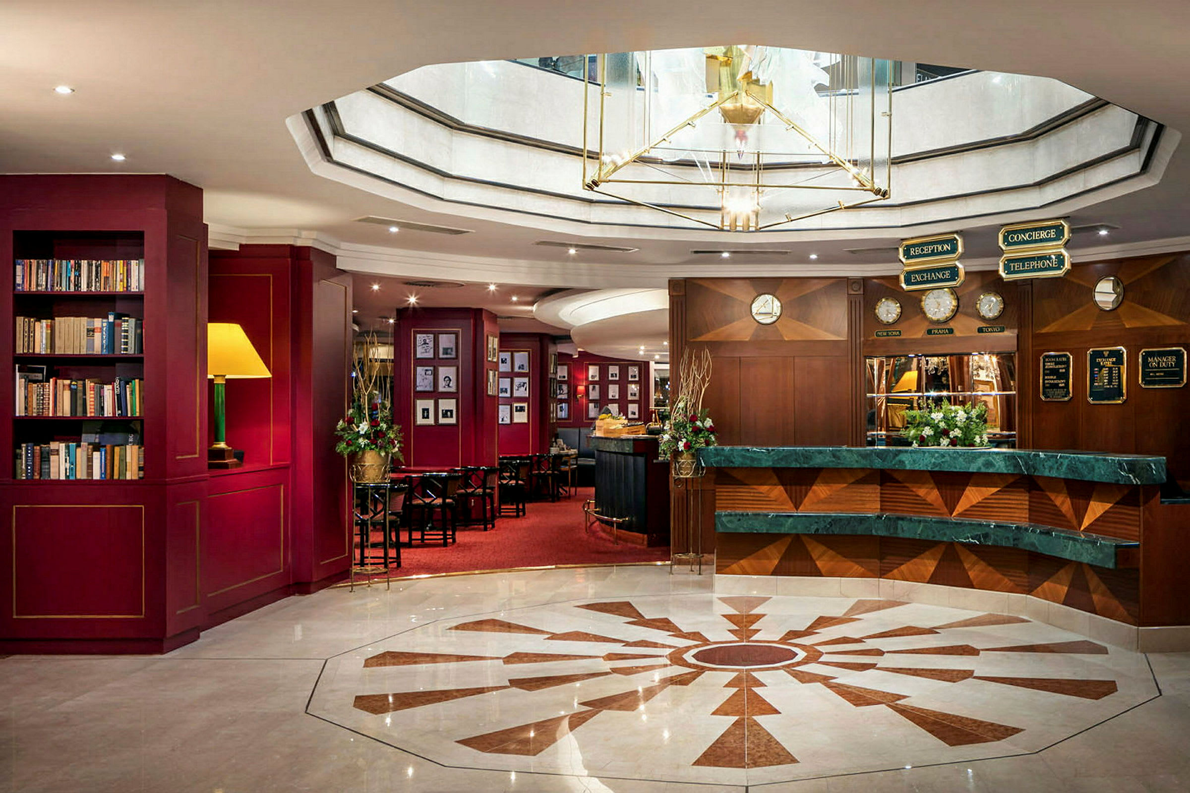 Ett hotellobbyområde med reception och bibliotek. Inredningen är elegant med rika färger och en central takkrona. (AI-genererad text)