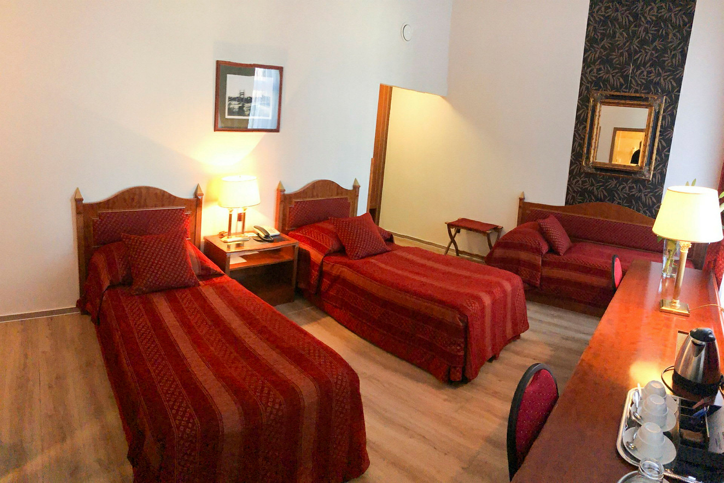 Hotellrum med tre sängar i ett rymligt inrett utrymme, dekorerade med röda textilier och trädetaljer. (AI-genererad text)