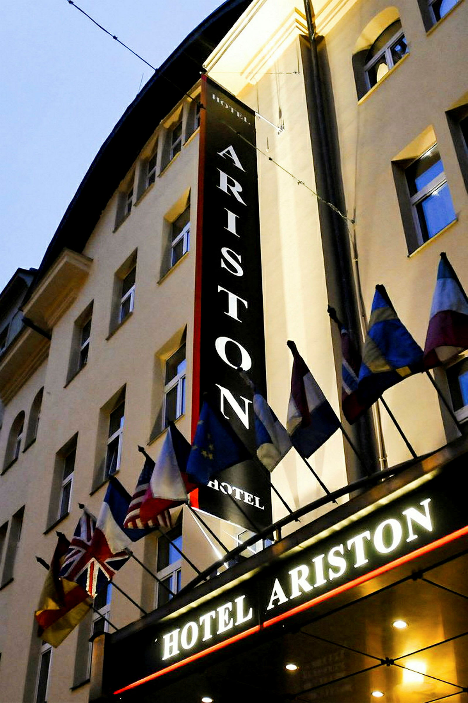 En hotellbyggnad med skyltar som säger 'Hotel Ariston' och ett antal nationalflaggor ovanför entrén. (AI-genererad text)