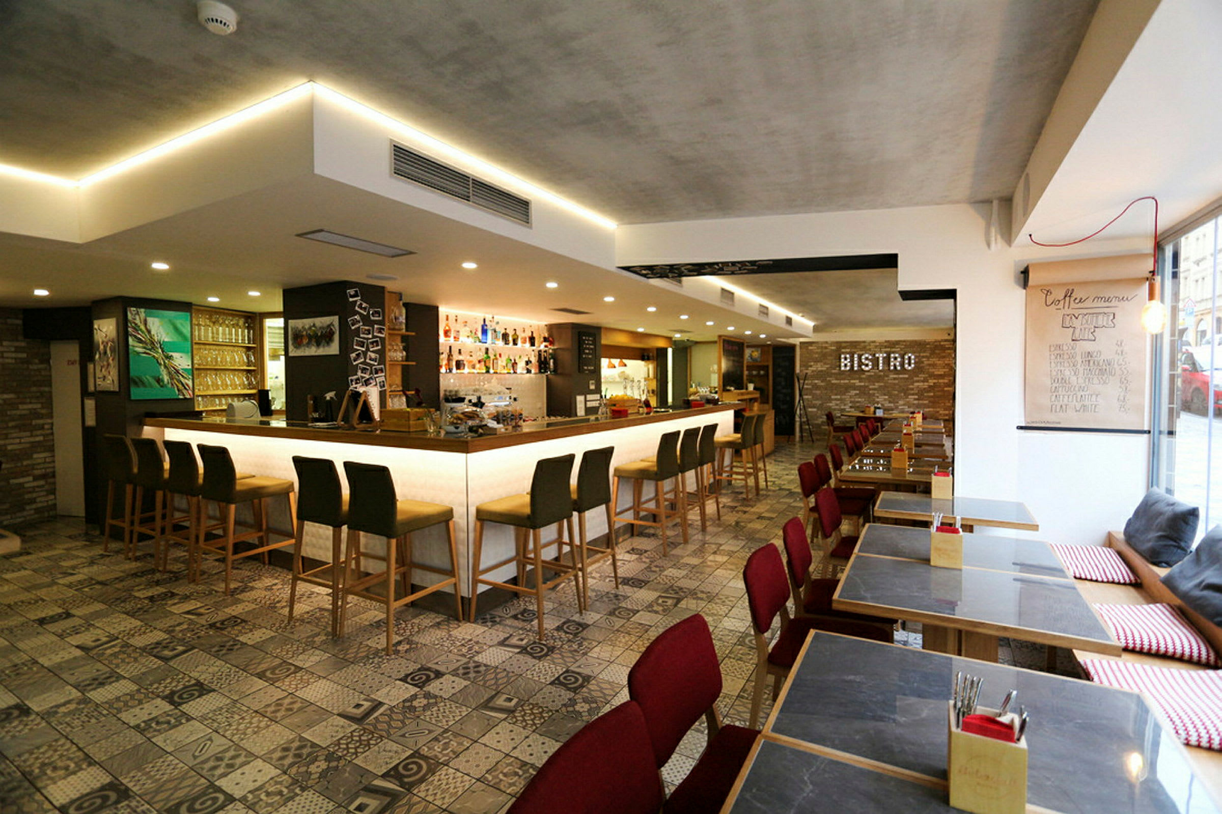 Interiör av en modern bistro med barstolar framför en upplyst bardisk och matbord med röda stolar. (AI-genererad text)