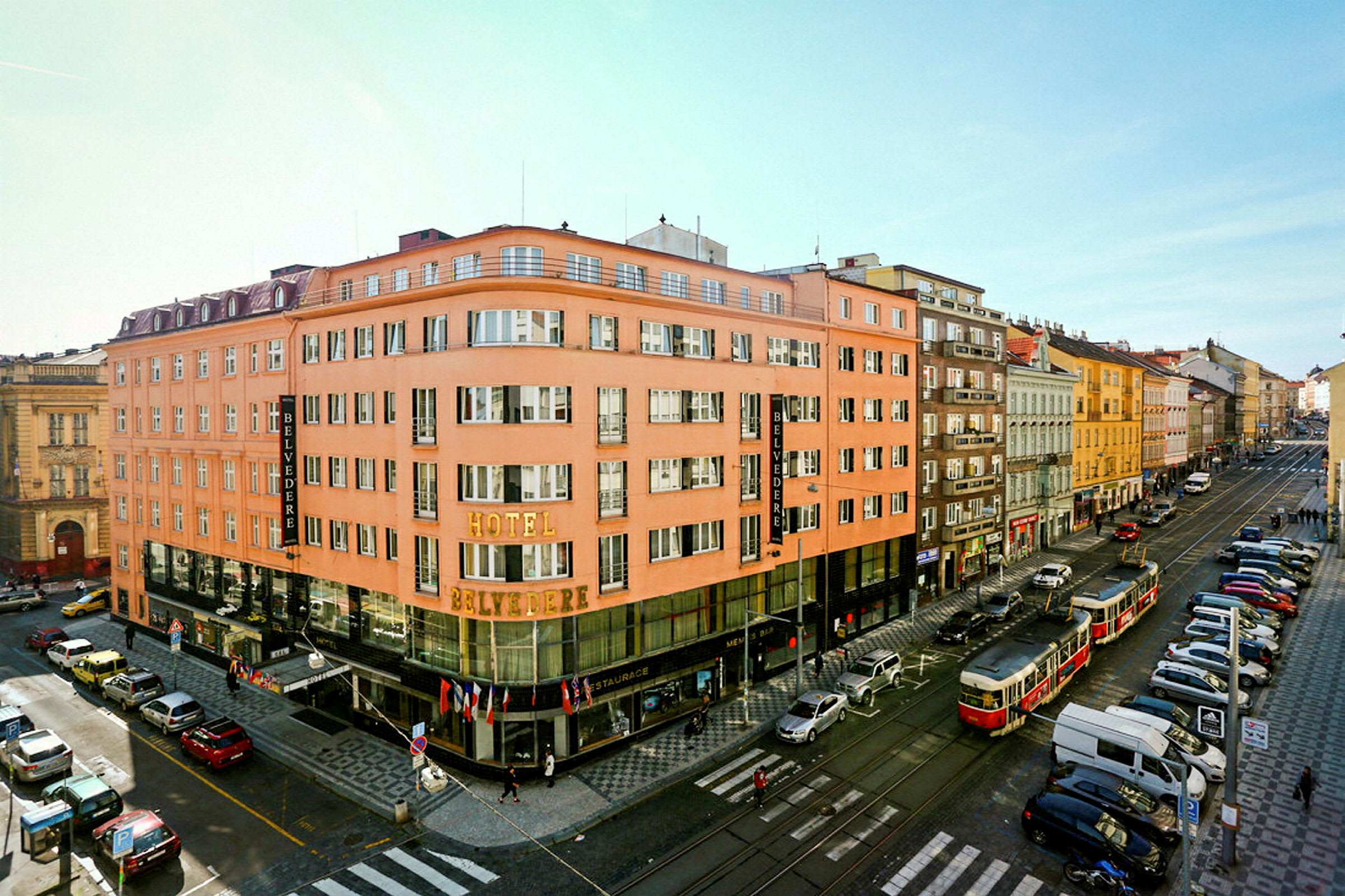 En stadsvy med ett rosa hotell kallat Belvedere längst fram på hörnet, omgiven av gator och parkerade bilar. (AI-genererad text)