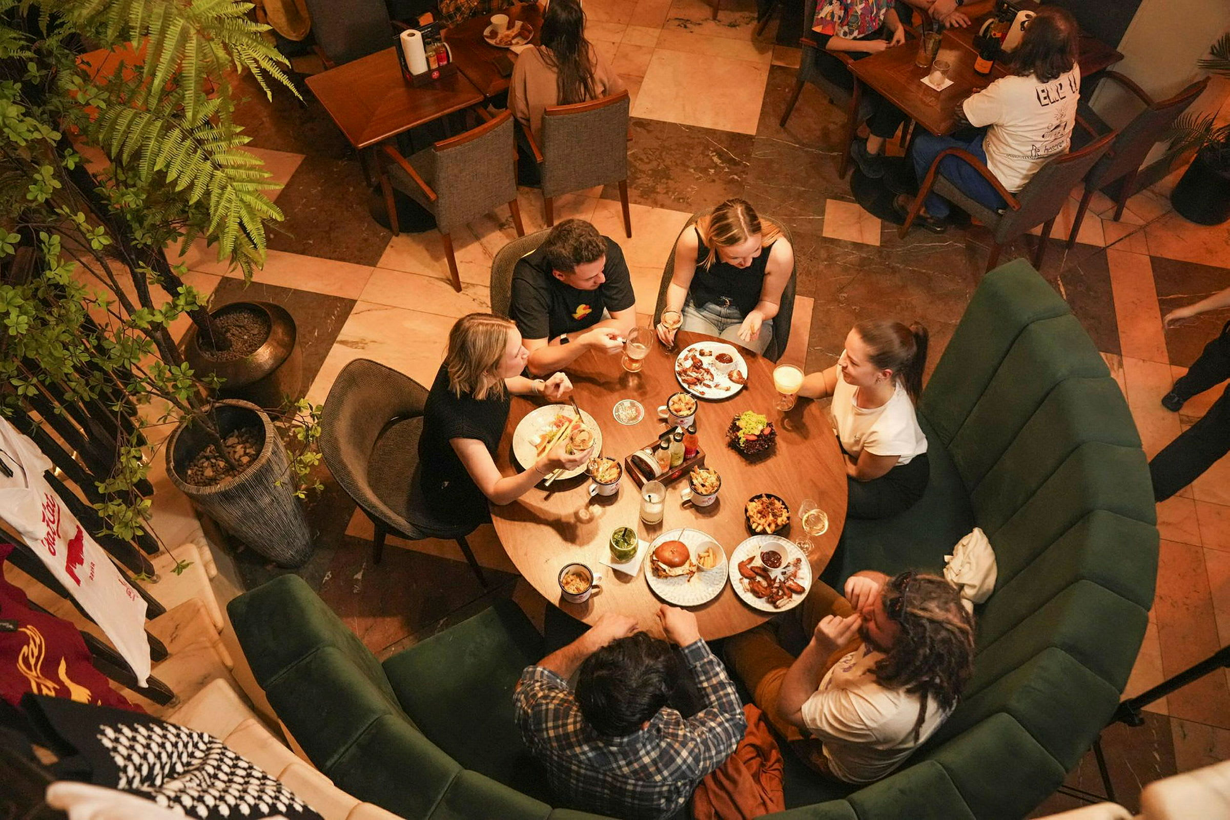 Fem personer sitter runt ett runt bord på en restaurang och äter och dricker. (AI-genererad text)