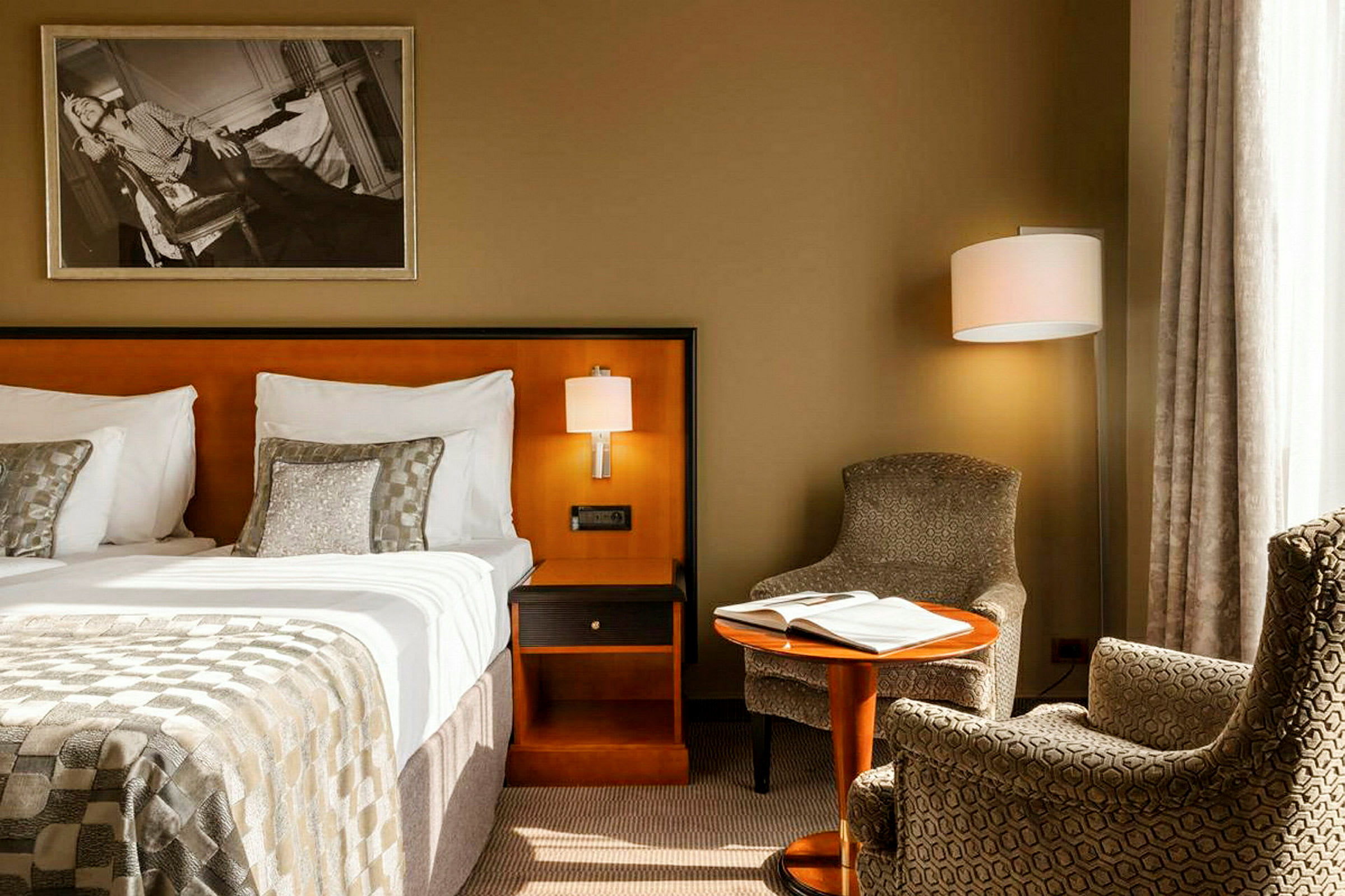 Ett hotellrum med en säng, nattduksbord, fåtöljer och ett litet bord med en bok på. (AI-genererad text)