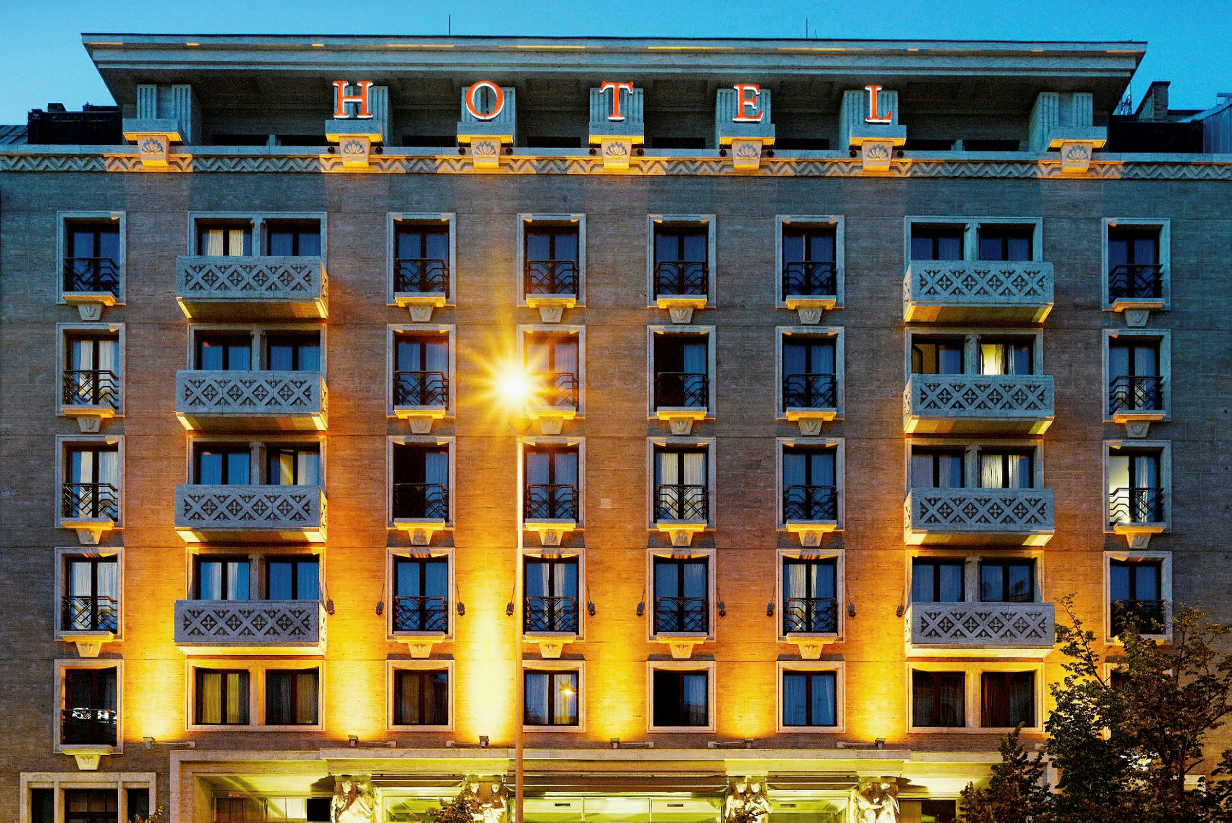 En flerfärgad hotellbyggnad med balkonger och stort upplyst skyltskription "HOTEL" på toppen. (AI-genererad text)