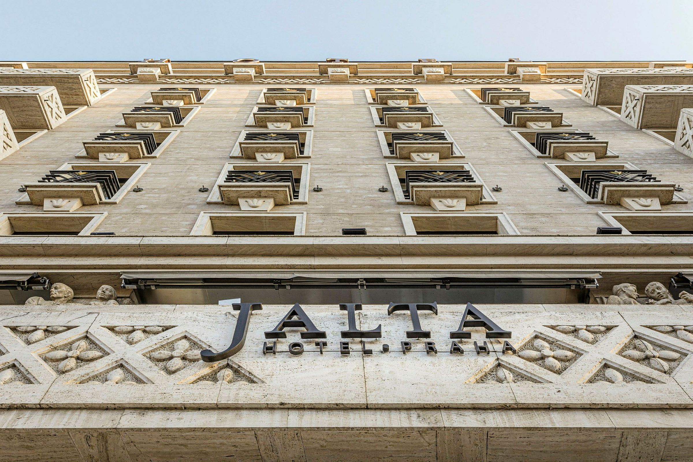 En byggnad fasad fotograferad nerifrån och upp, med en skylt där det står "Jalta Hotel Praha". (AI-genererad text)