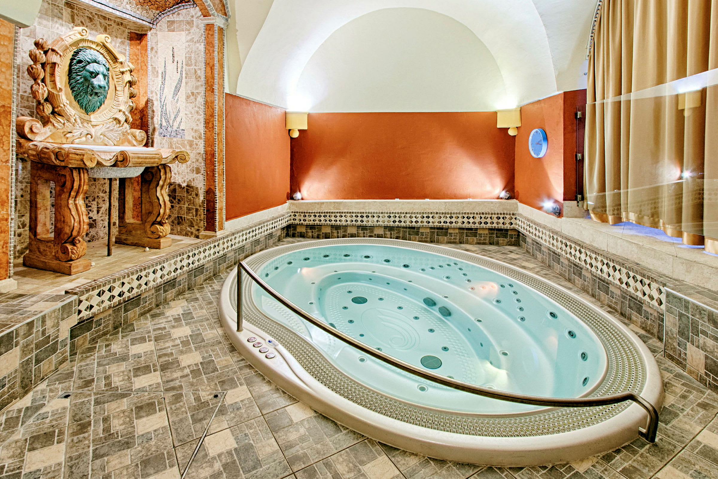 En inomhus jacuzzi med mosaik och dekorativ ornamentering på väggarna och golvet. (AI-genererad text)