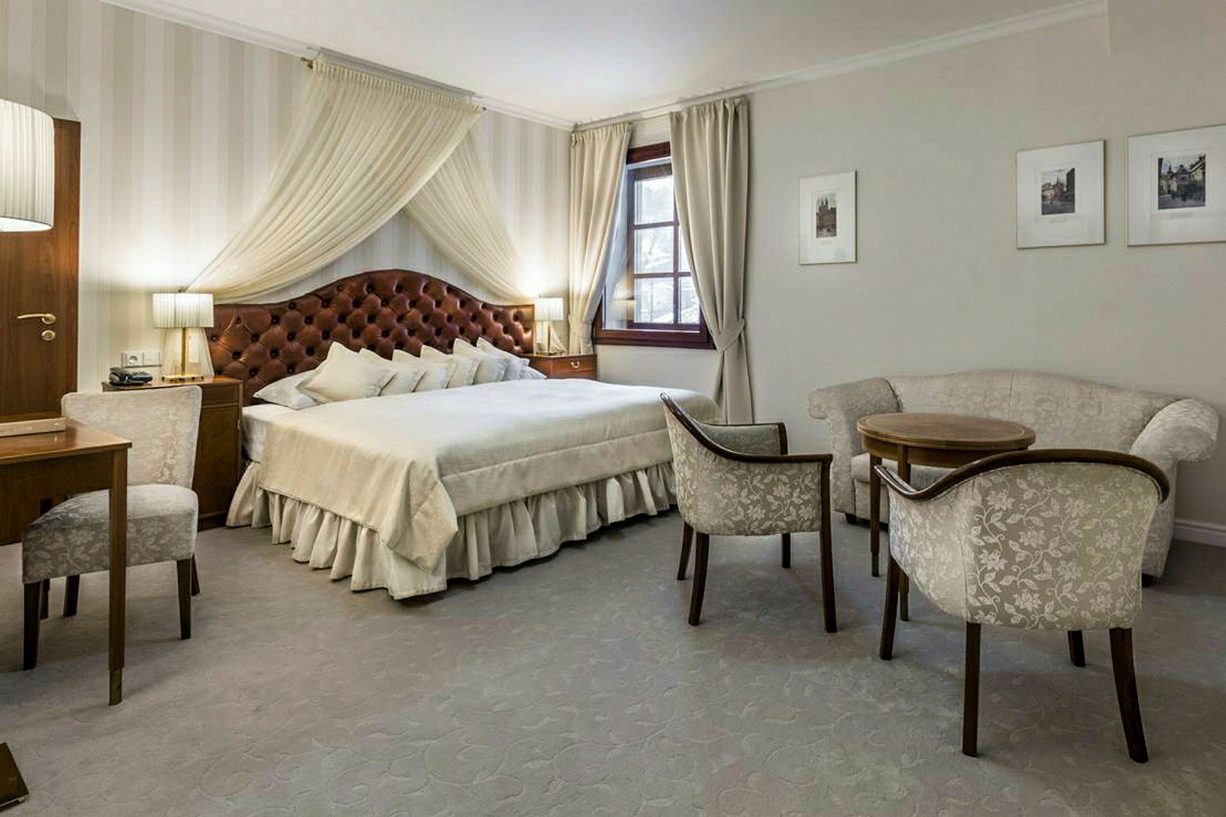 Ett elegant inrett sovrum med en stor dubbelsäng, bekväma sittmöbler, ett skrivbord och fönster med gardiner. (AI-genererad text)