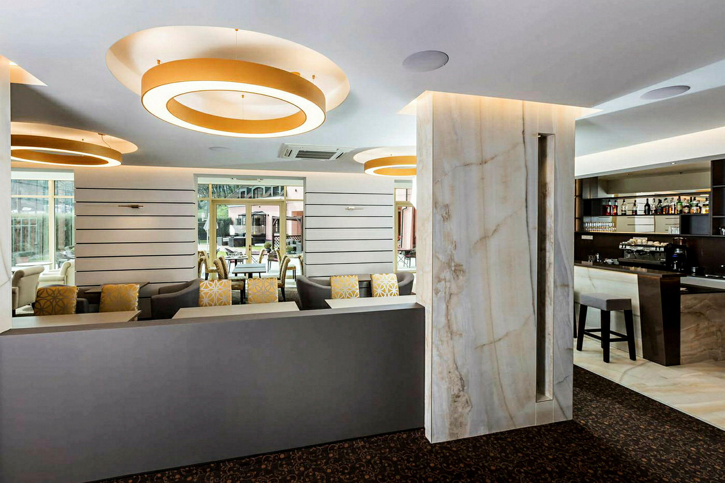 Interiör av en modern lounge med soffor, barområde och stora dekorerande ljusringar i taket. (AI-genererad text)