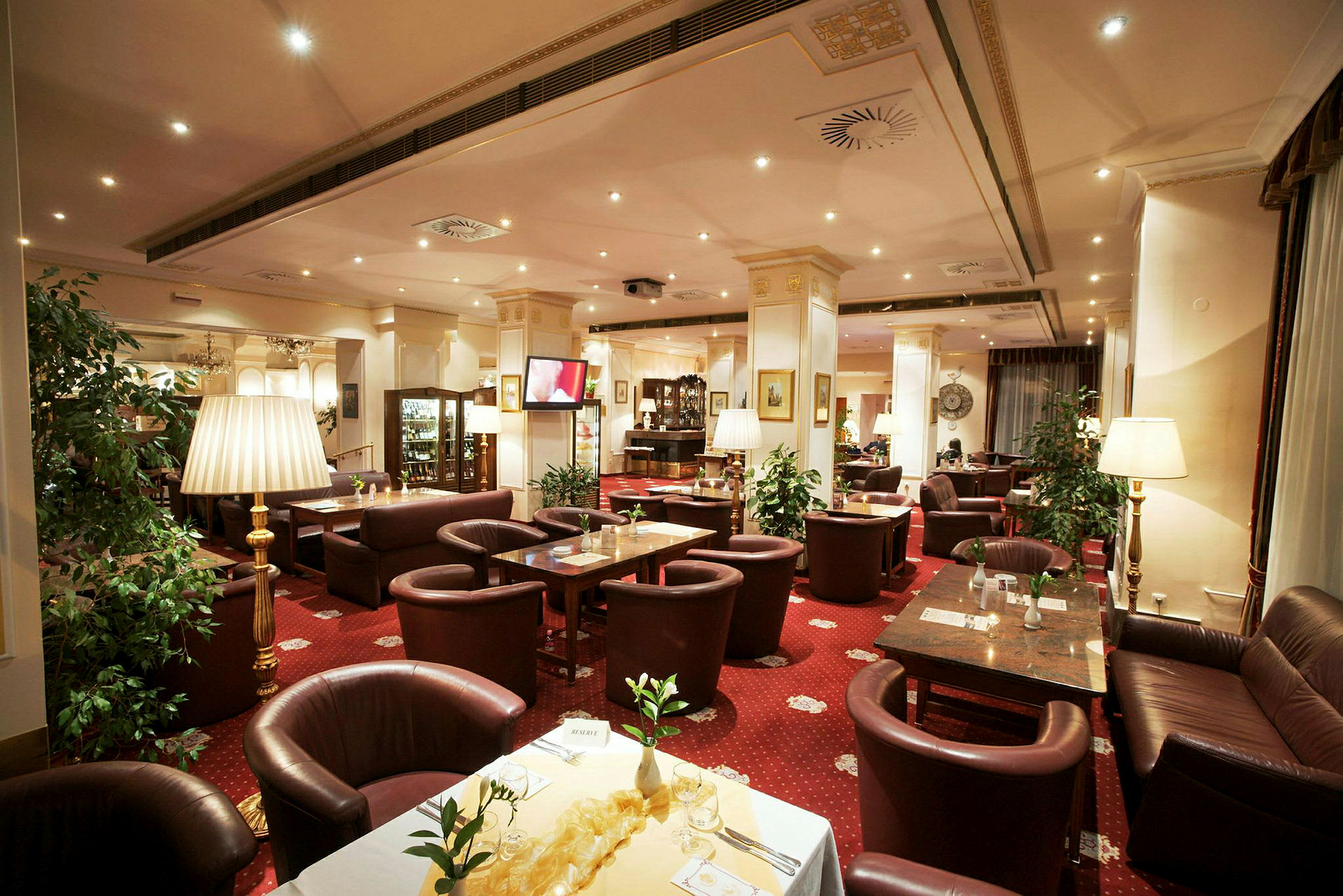 Bild av en elegant restaurang med röda mattor, bruna lädersoffor och stolar samt dekorerade bord. (AI-genererad text)
