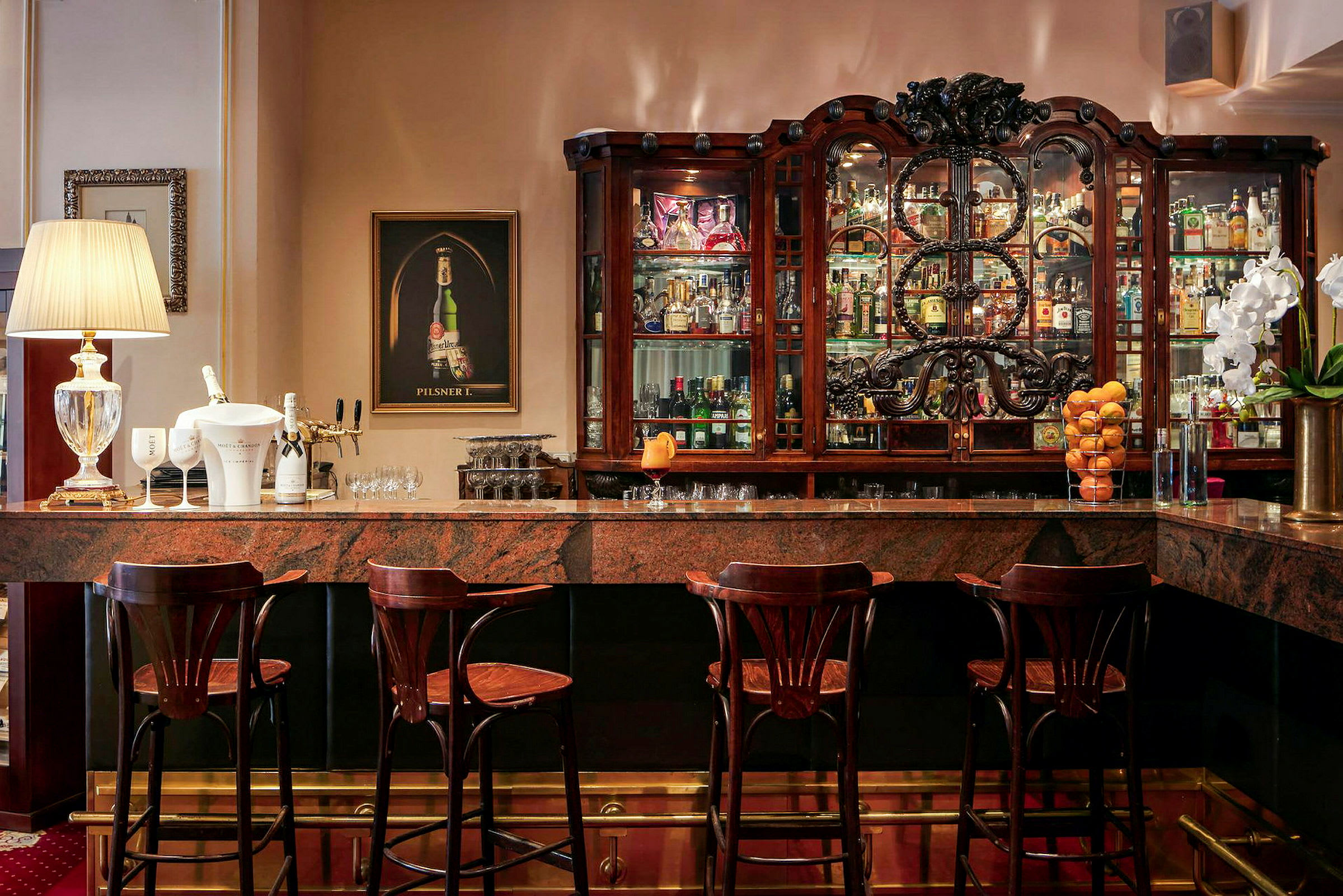 En elegant bar med marmordisk, trästolar, en utsmyckad hylla fylld med flaskor och dekorationer, samt belysning. (AI-genererad text)