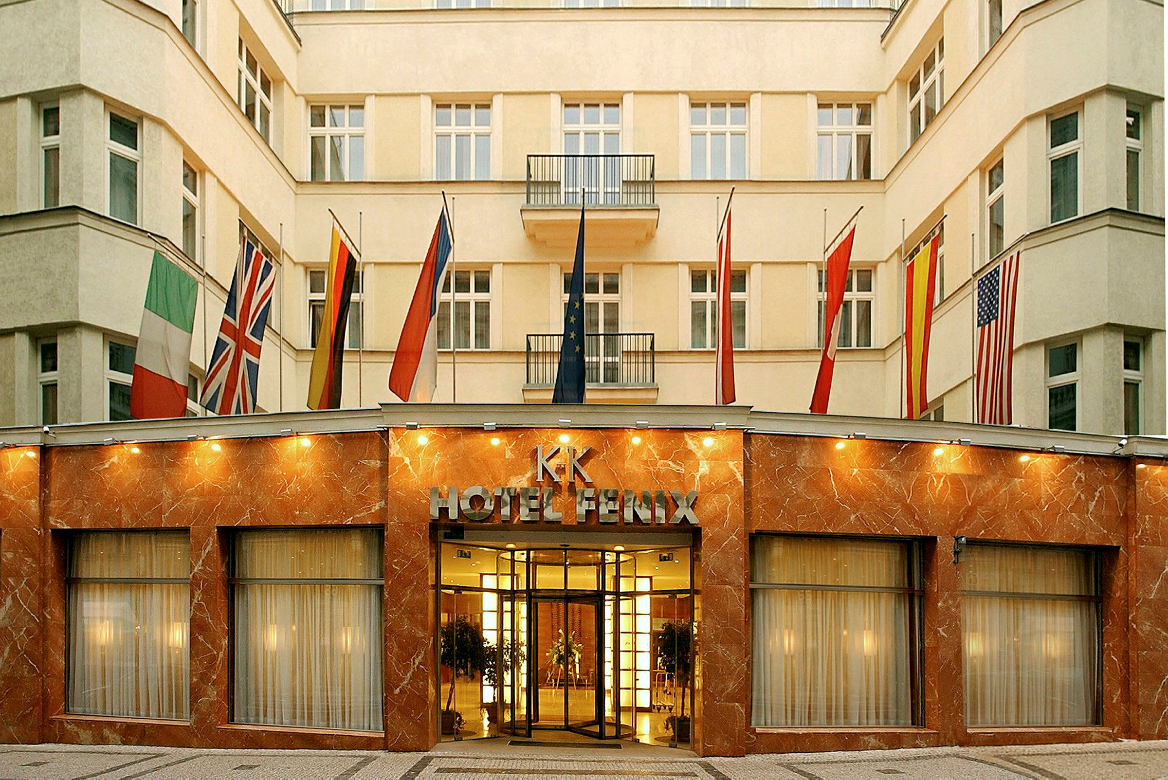Byggnaden är ett hotell med fasad av marmor och glas samt flera flaggor vid entrén. (AI-genererad text)