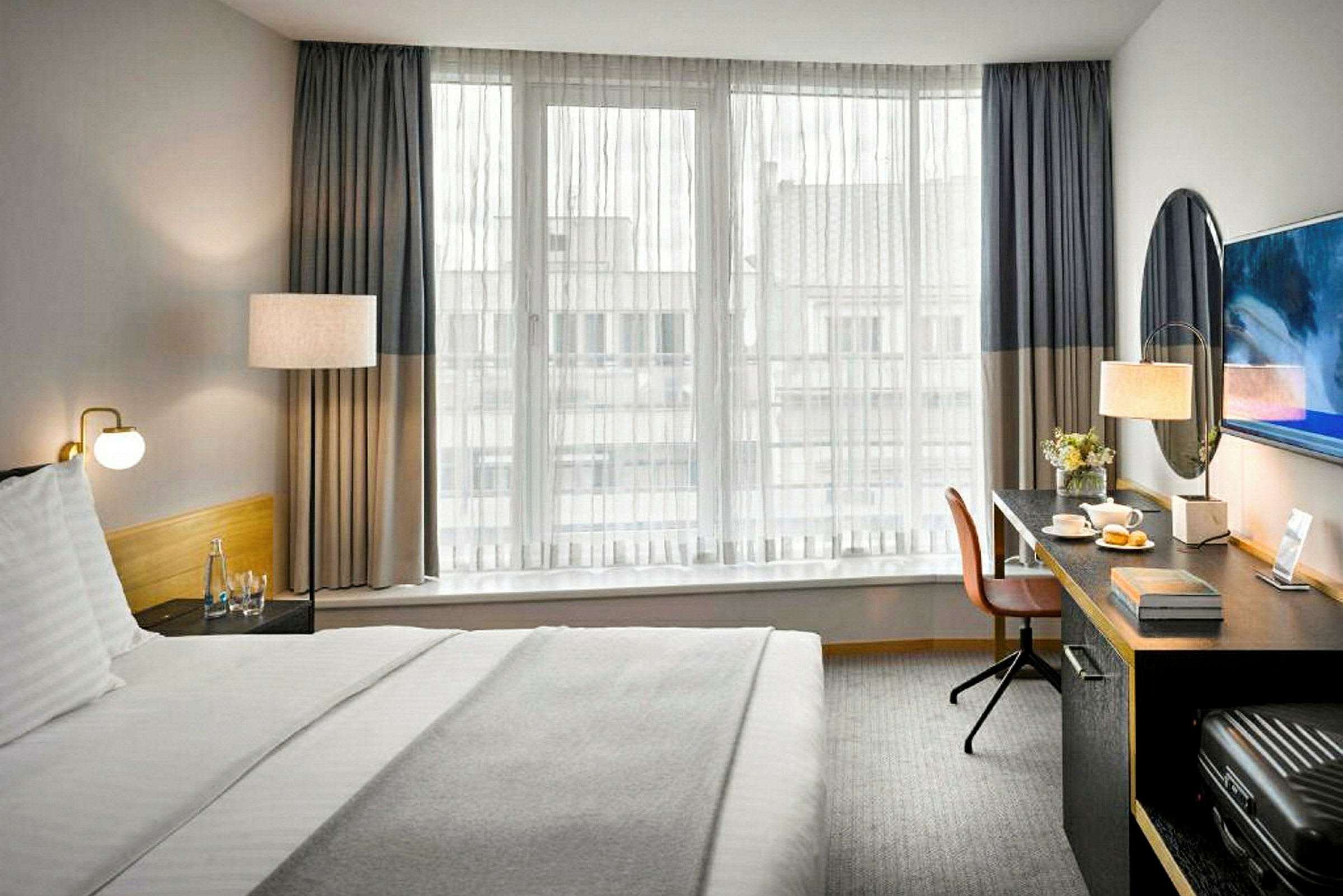 Ett hotellrum med en säng, ett skrivbord och ett fönster med tunna gardiner. (AI-genererad text)
