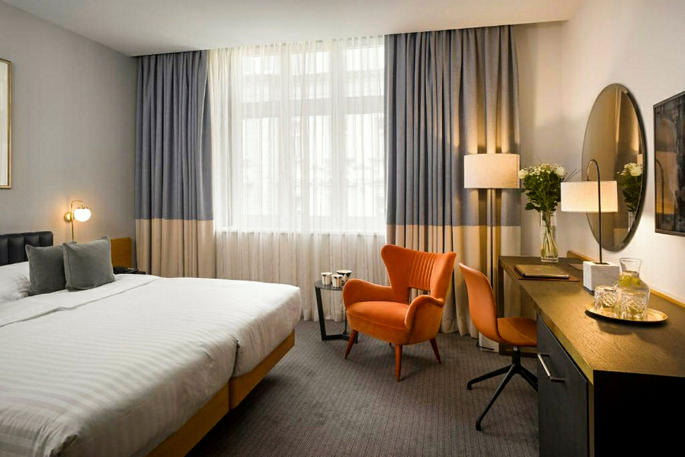Ett hotellrum med en stor säng, en orange fåtölj och skrivbord med spegel. (AI-genererad text)