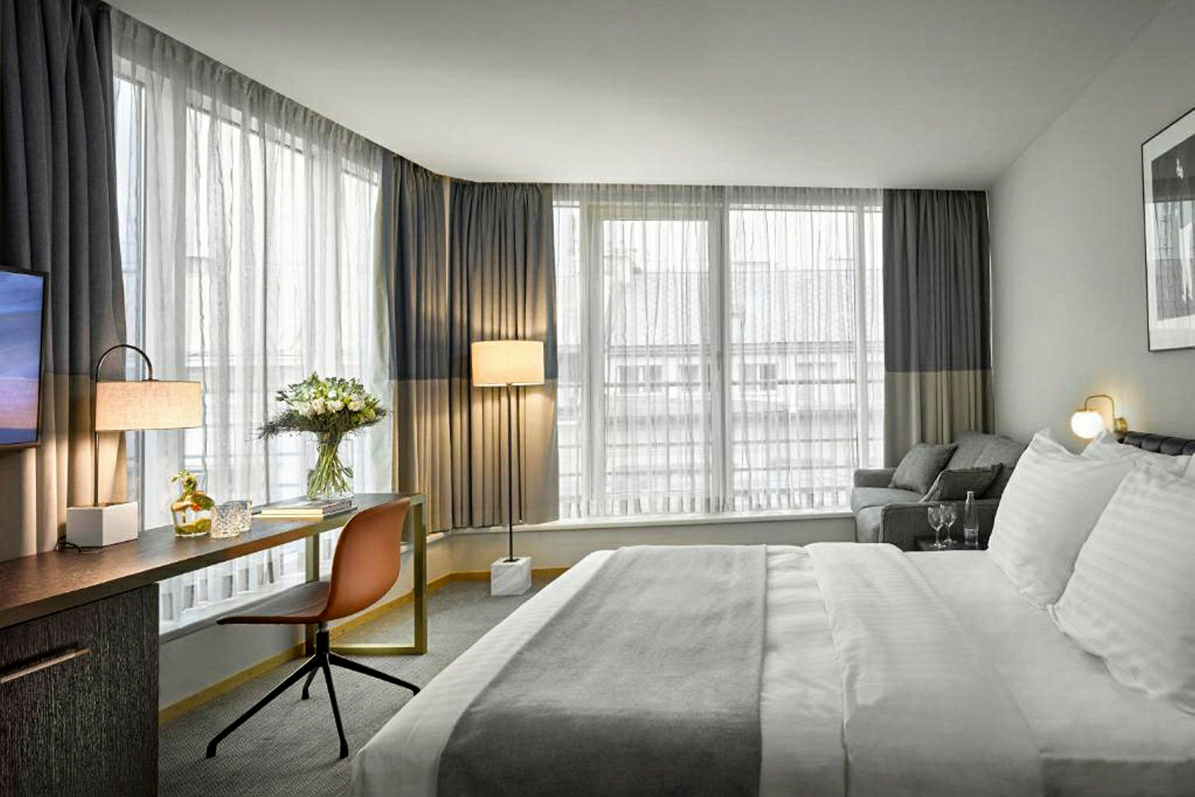 Ett hotellrum med stor säng, skrivbord, stol och fönster med gardiner. (AI-genererad text)