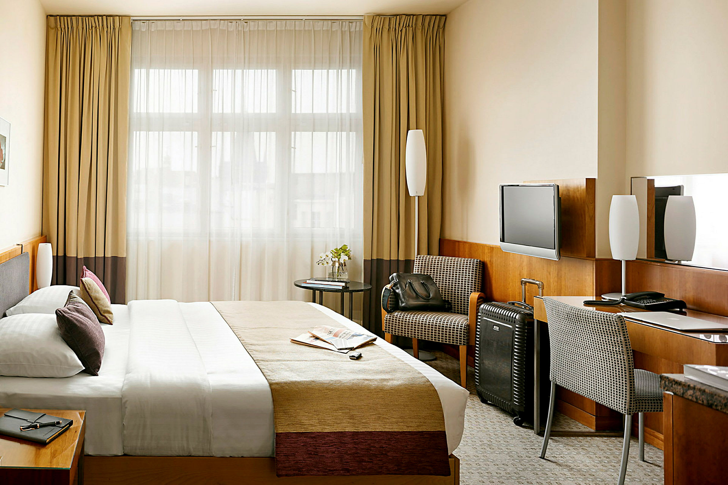 Ett hotellrum med en stor säng, skrivbord och stol, samt en fåtölj och en resväska. (AI-genererad text)