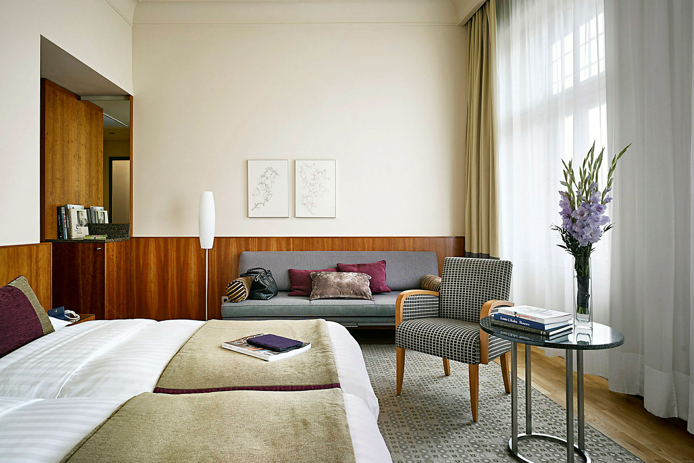 Ett hotellrum med en säng, en soffa, en fåtölj och ett bord med en vas med blommor. (AI-genererad text)