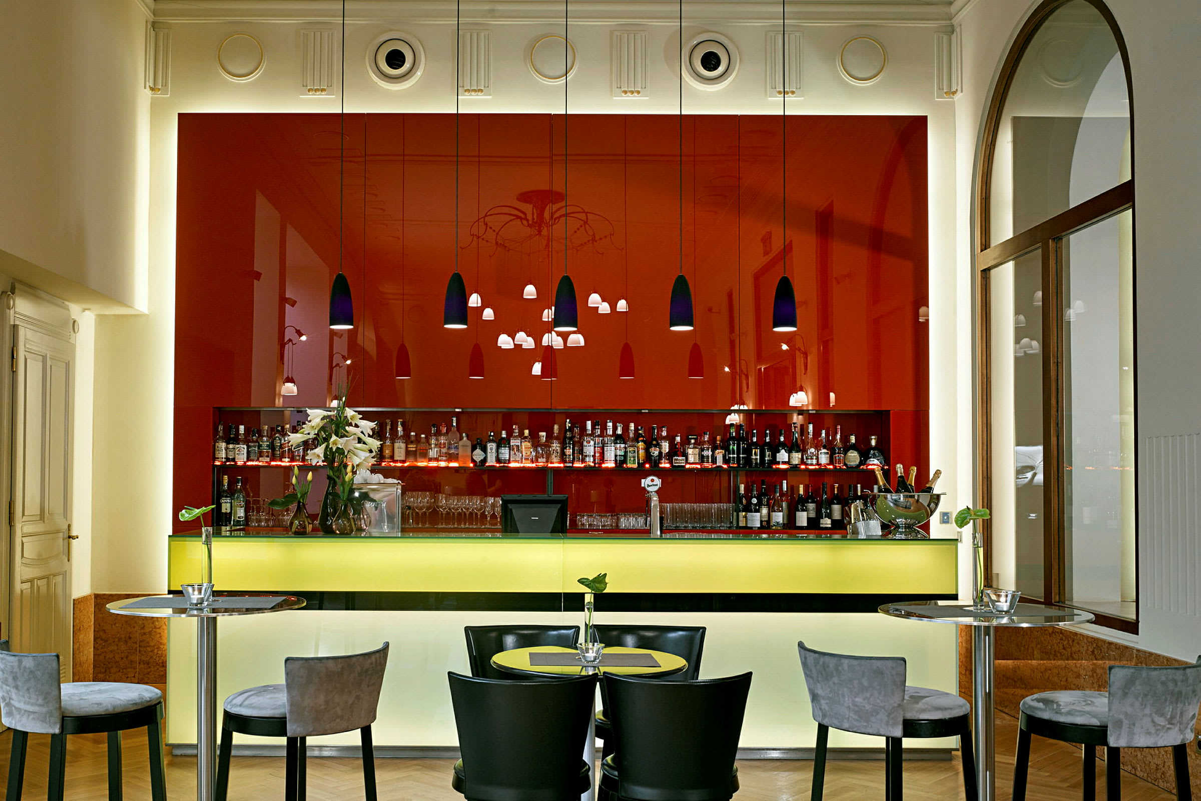 En modern bar med röda väggar och en upplyst gul bardisk, omgiven av stolar och bord. (AI-genererad text)