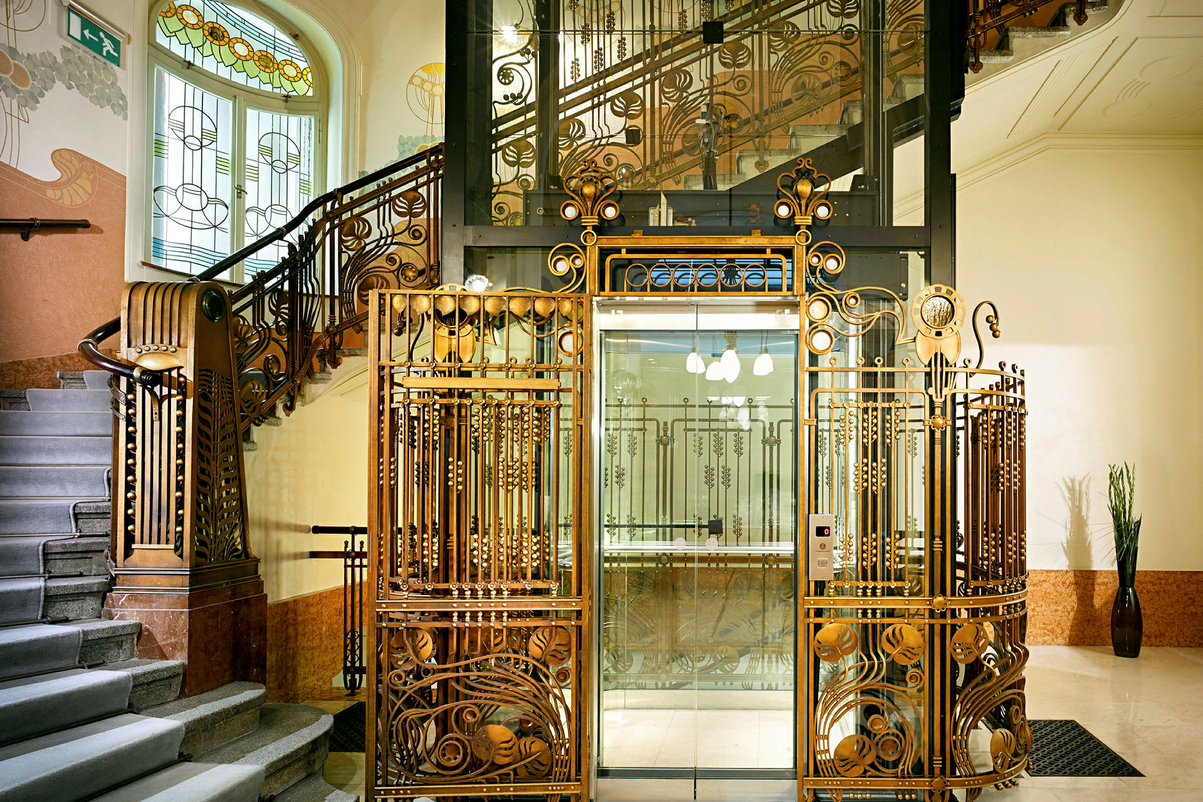 En vacker Art Nouveau-trappa med dekorerade järnräcken samt en glasad hiss inramad av ett dekorerat metallstaket. (AI-genererad text)
