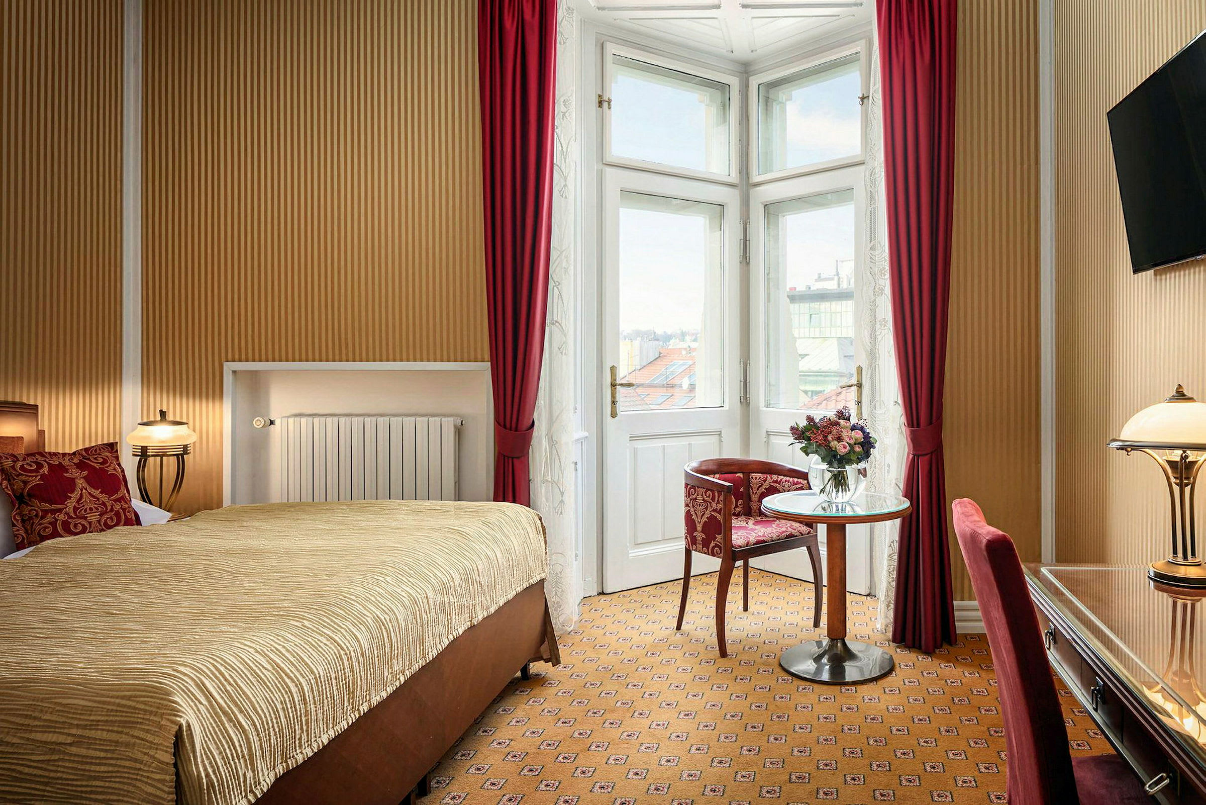Bild av ett hotellrum med en stor säng, ett litet bord och en stol bredvid ett stort fönster med röda gardiner. (AI-genererad text)