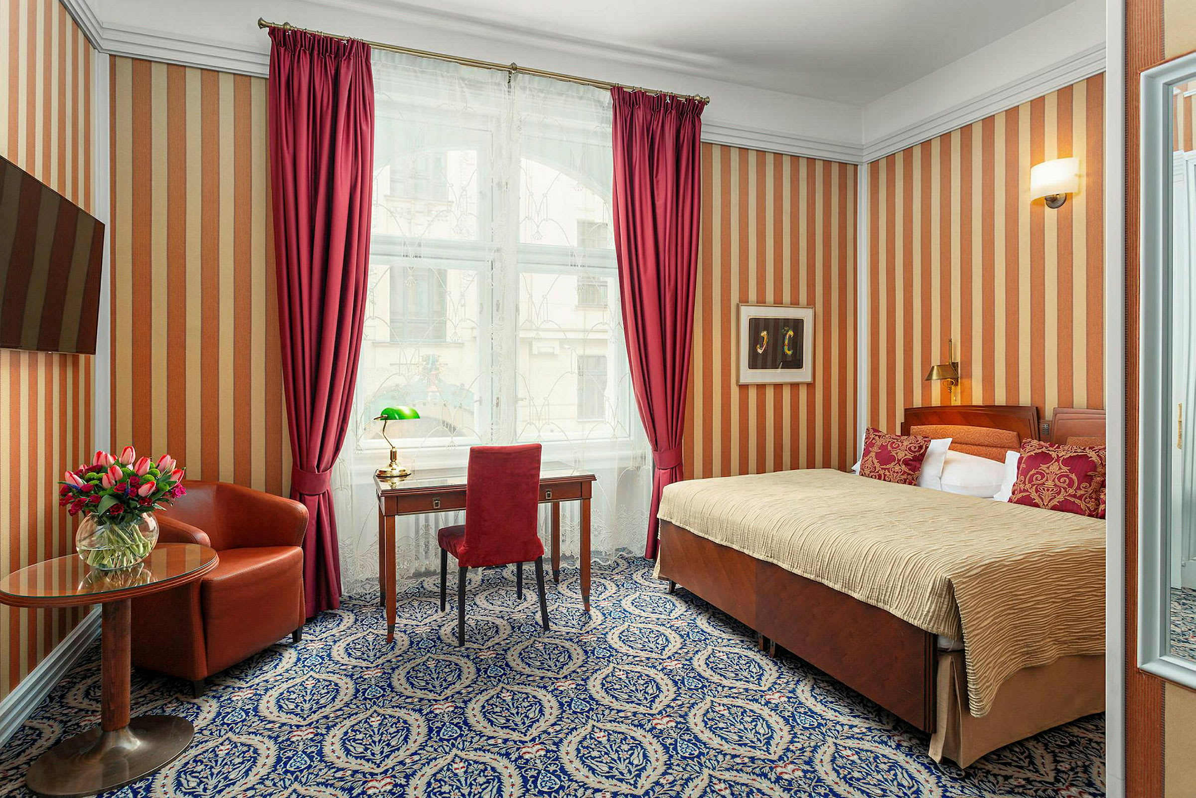 Ett hotellrum med en säng, skrivbord, fåtölj och ett runt bord med en vas med blommor. (AI-genererad text)