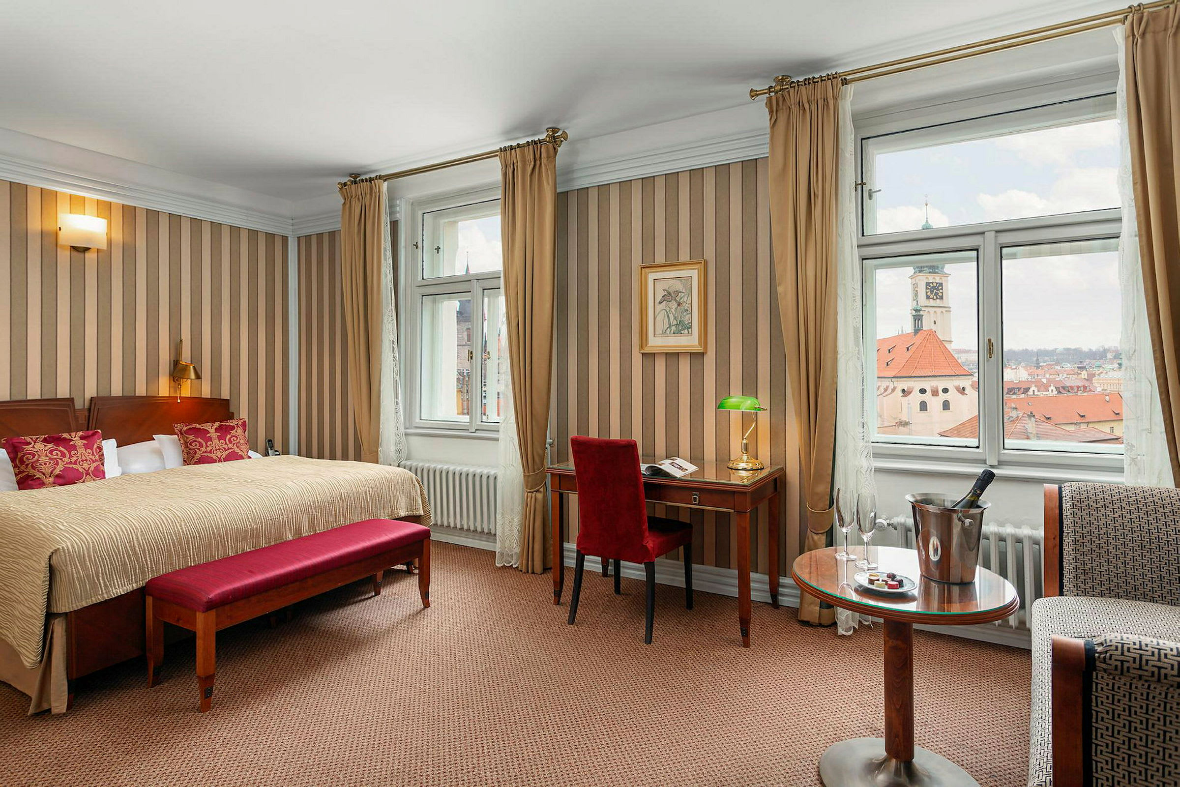 Ett hotellrum med stor säng, skrivbord, och utsikt över stadens tak genom fönstren. (AI-genererad text)