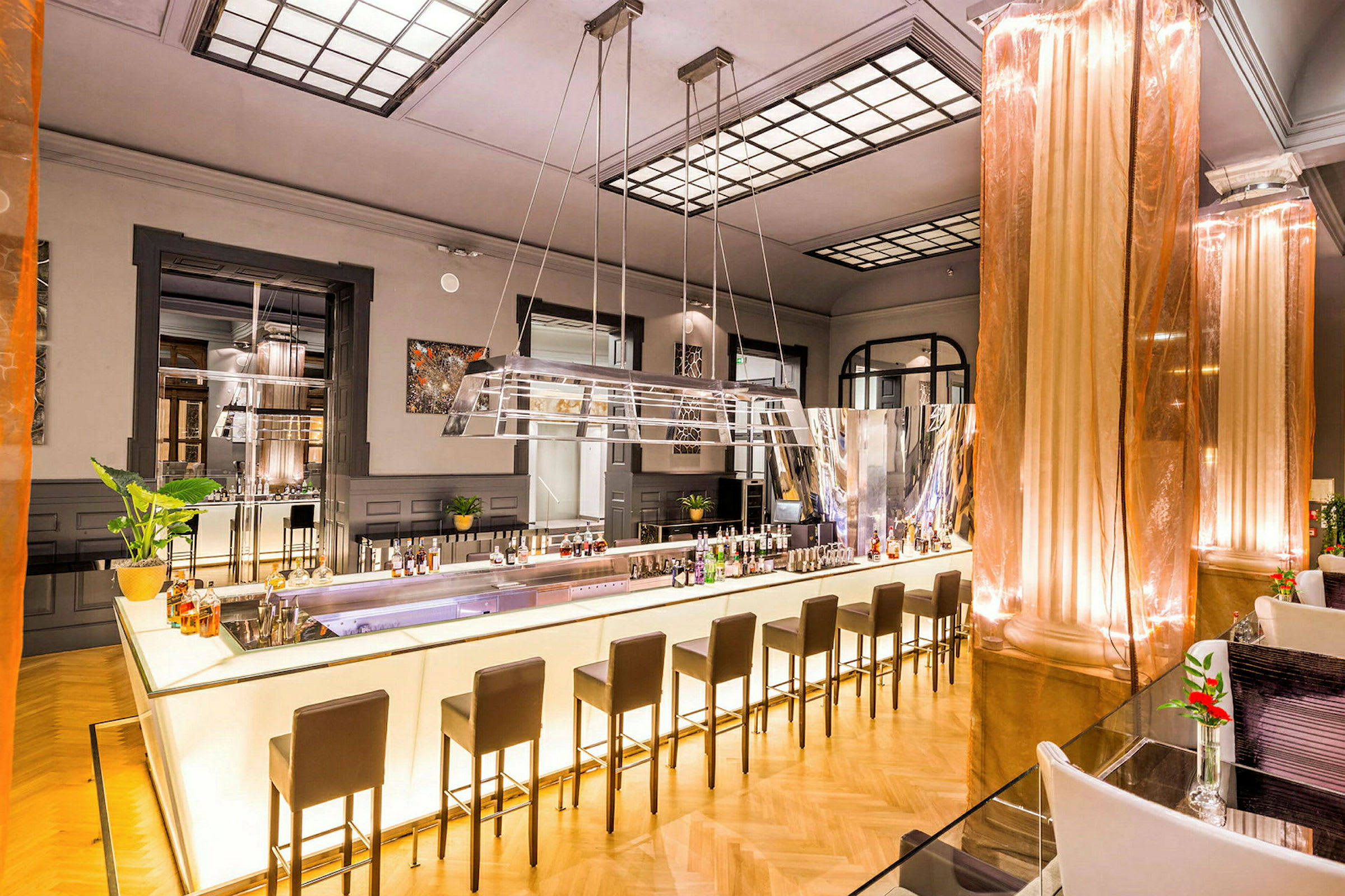 Bild på en modern bar med ljus belysning. Baren har höga stolar och är dekorerad med flaskor och växter. (AI-genererad text)