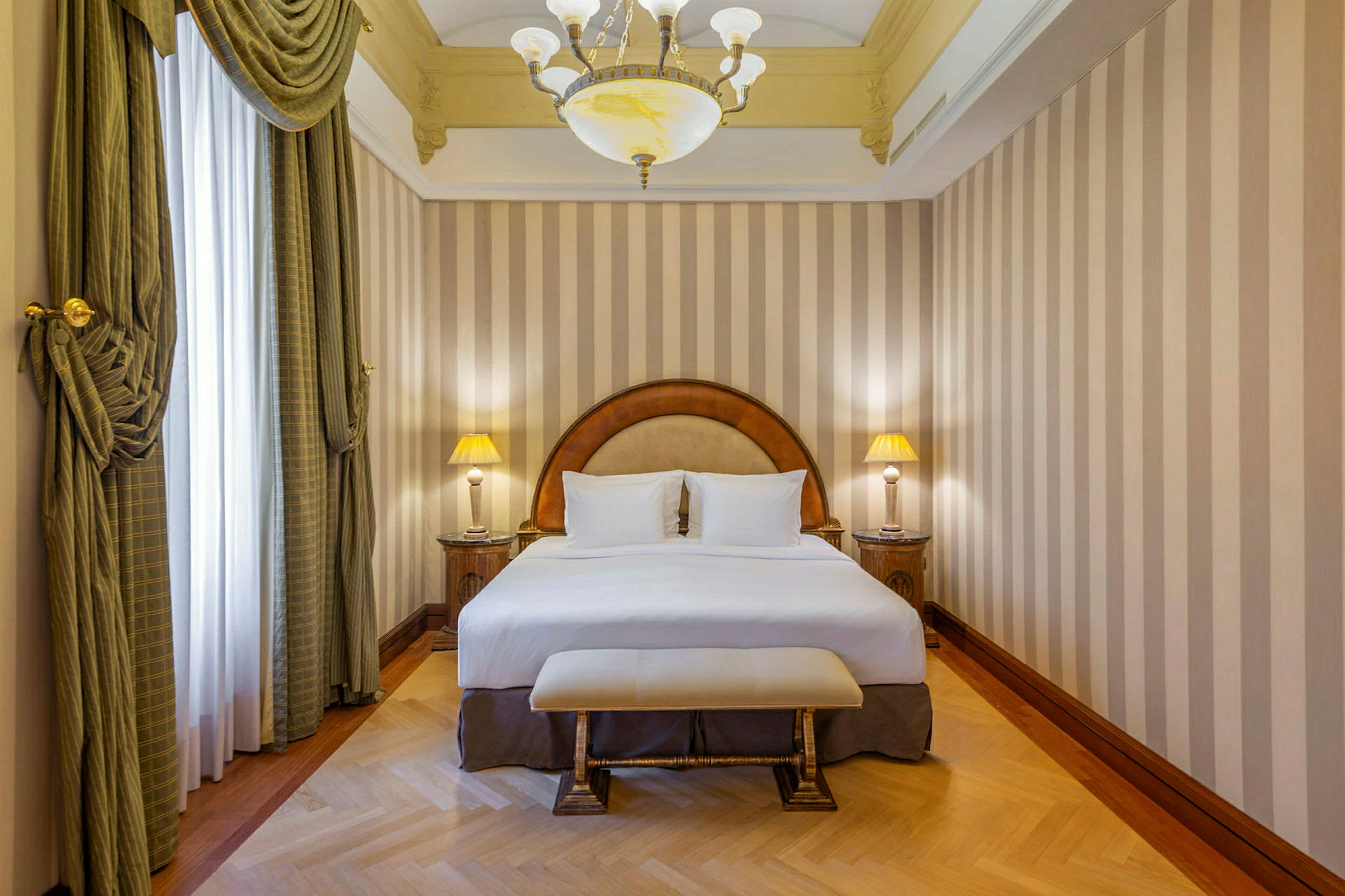 Ett hotellrum med en dubbelsäng, två sängbord med lampor, och eleganta gardiner framför fönstret. (AI-genererad text)