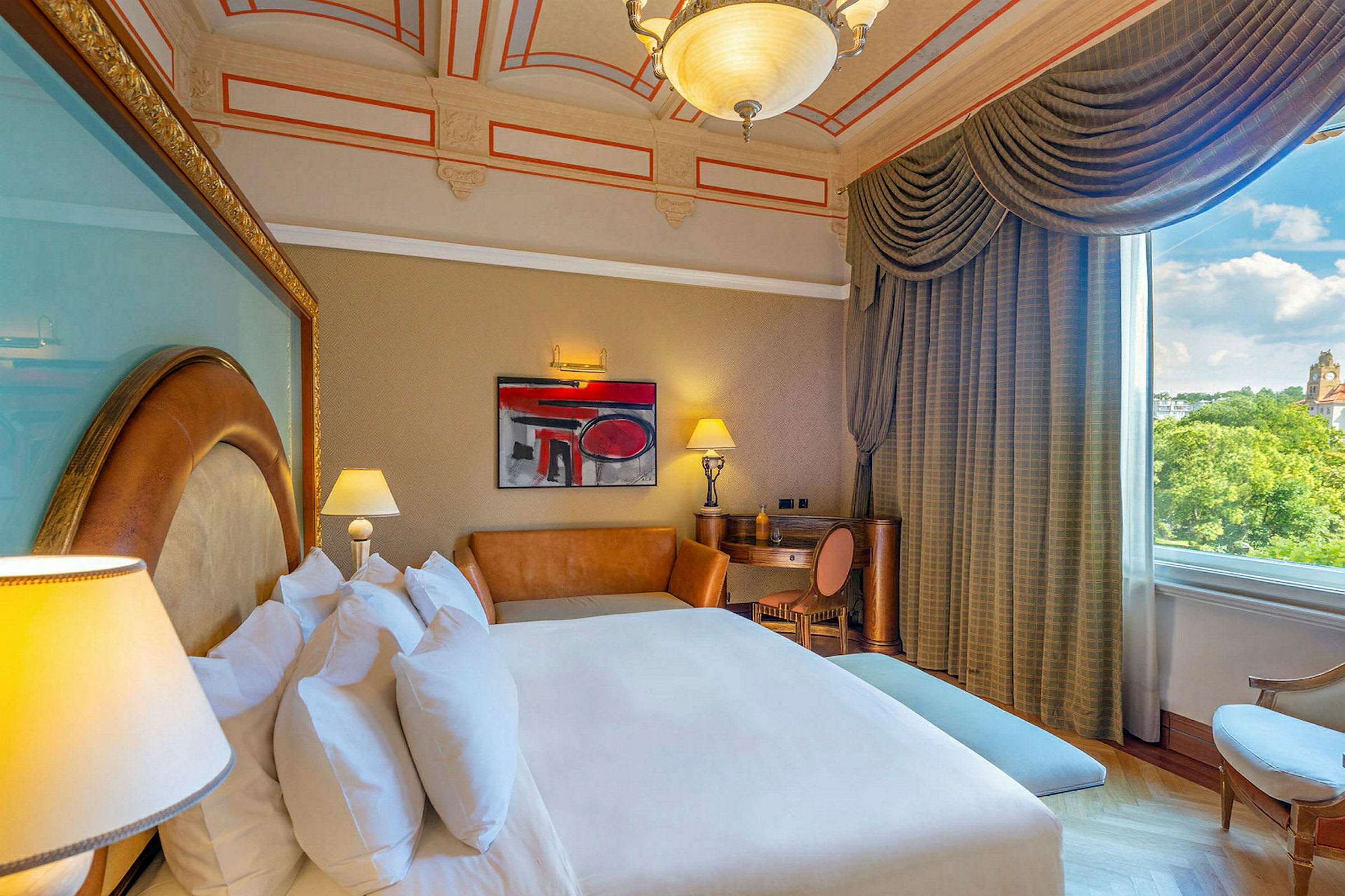 Ett hotellrum med en stor säng, soffmöbler, skrivbord och fönster med utsikt över grönska och byggnader. (AI-genererad text)