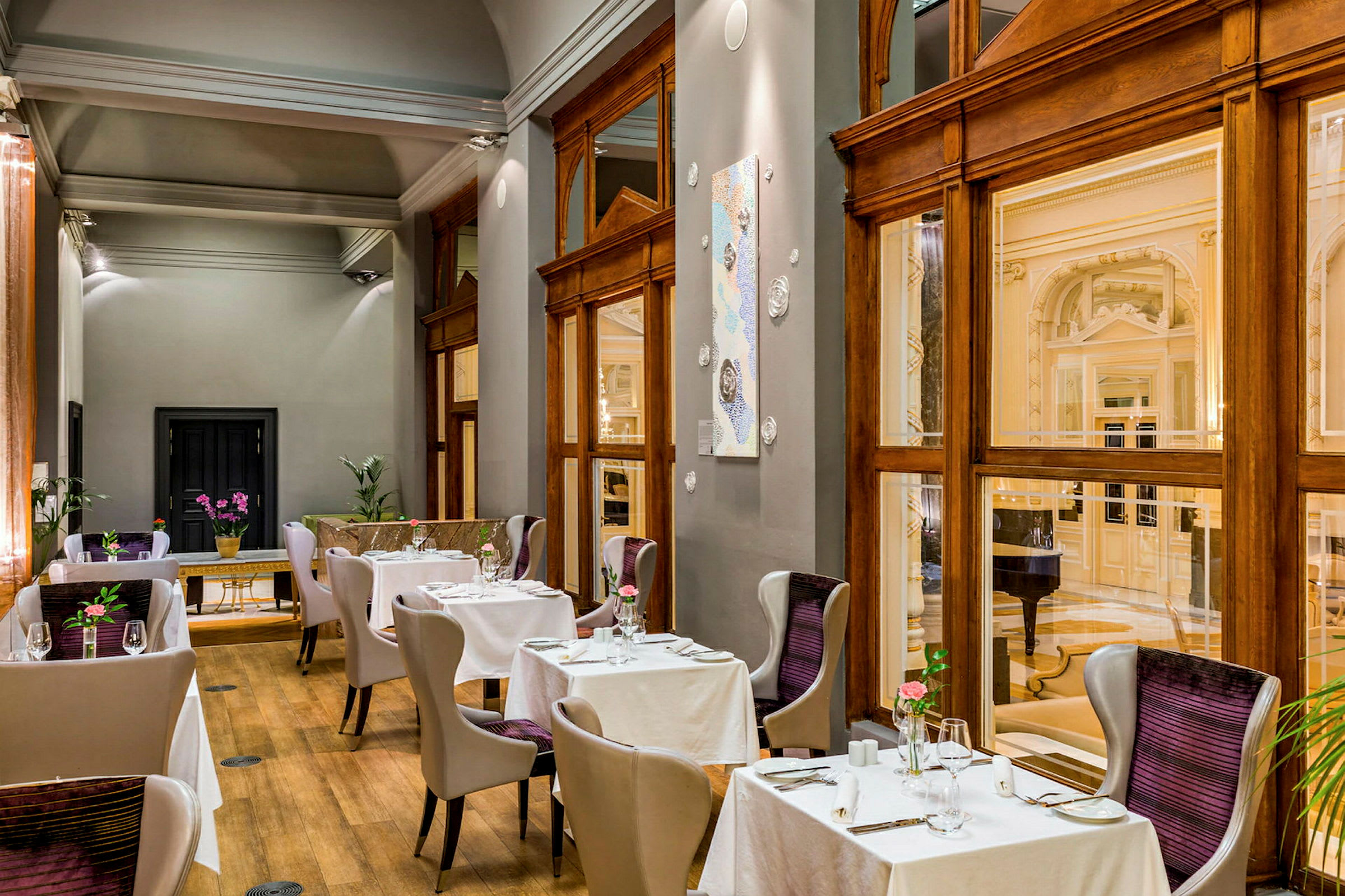 Bilden visar en elegant inredd restaurang med moderna stolar och bord klädda med vita dukar. Stora fönster och trädetaljer ger ett lyxigt intryck. (AI-genererad text)