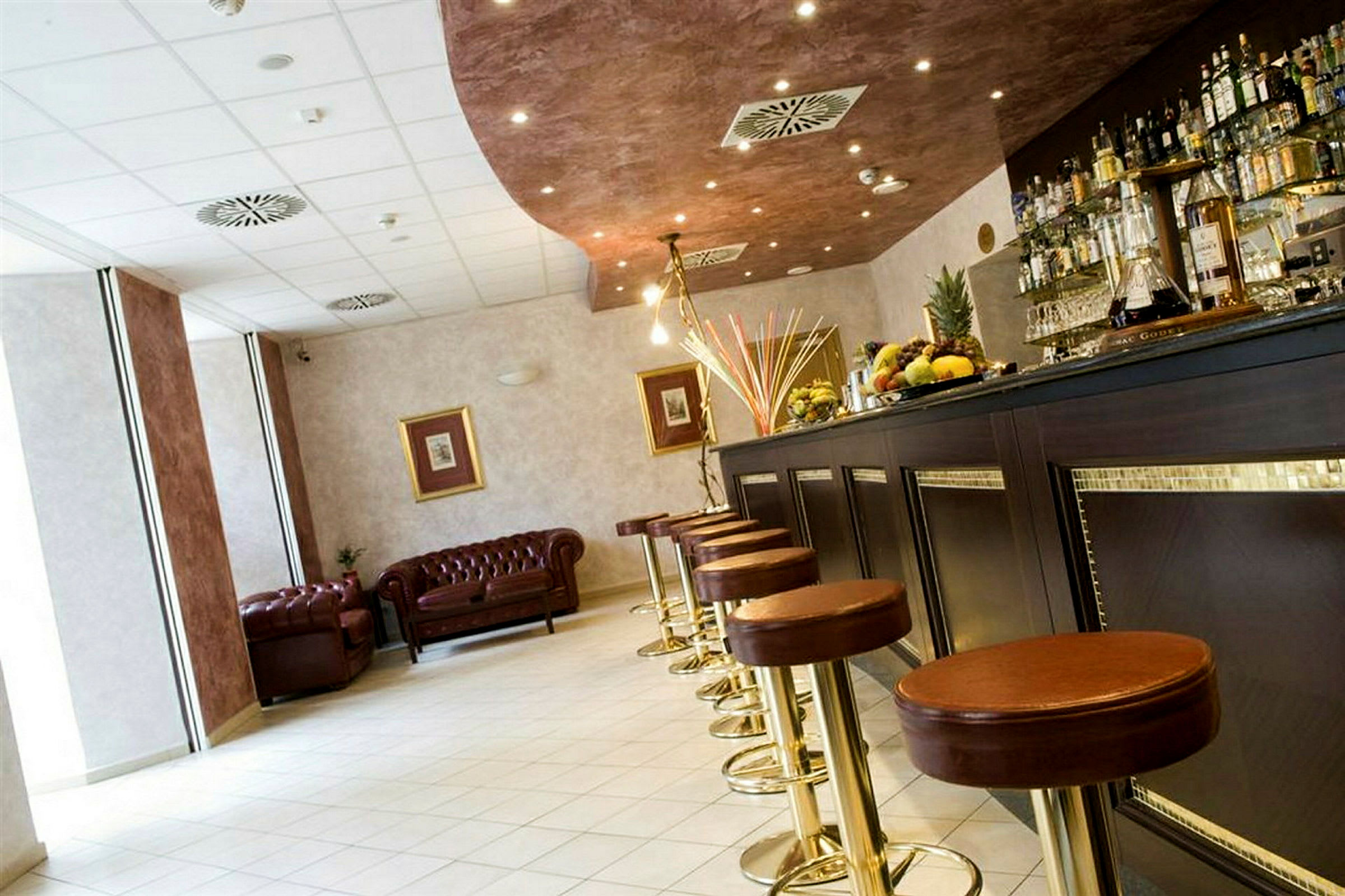 Bild av en hotellbar med höga stolar i läder, ett mörkt träbord och spritflaskor i hyllor. En sittgrupp med skinnsoffor syns i bakgrunden. (AI-genererad text)