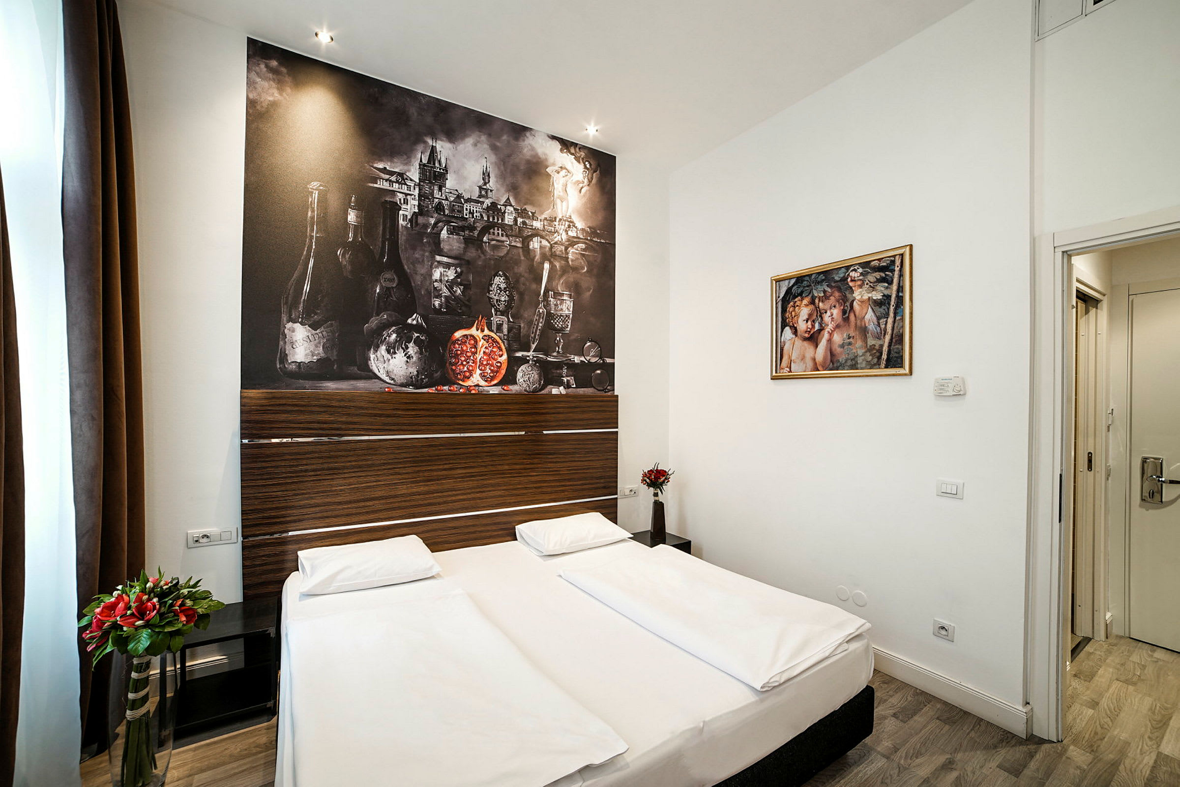 Ett hotellrum med en dubbelsäng, blomdekorationer och en stor väggkonst som föreställer stilleben. (AI-genererad text)