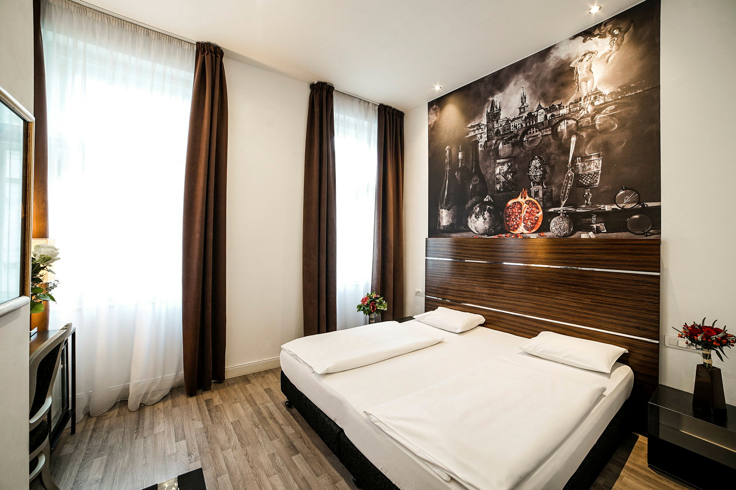 Ett hotellrum med en dubbelsäng, mörka gardiner, en dekorativ väggmålning samt möbler som bord och stol. (AI-genererad text)