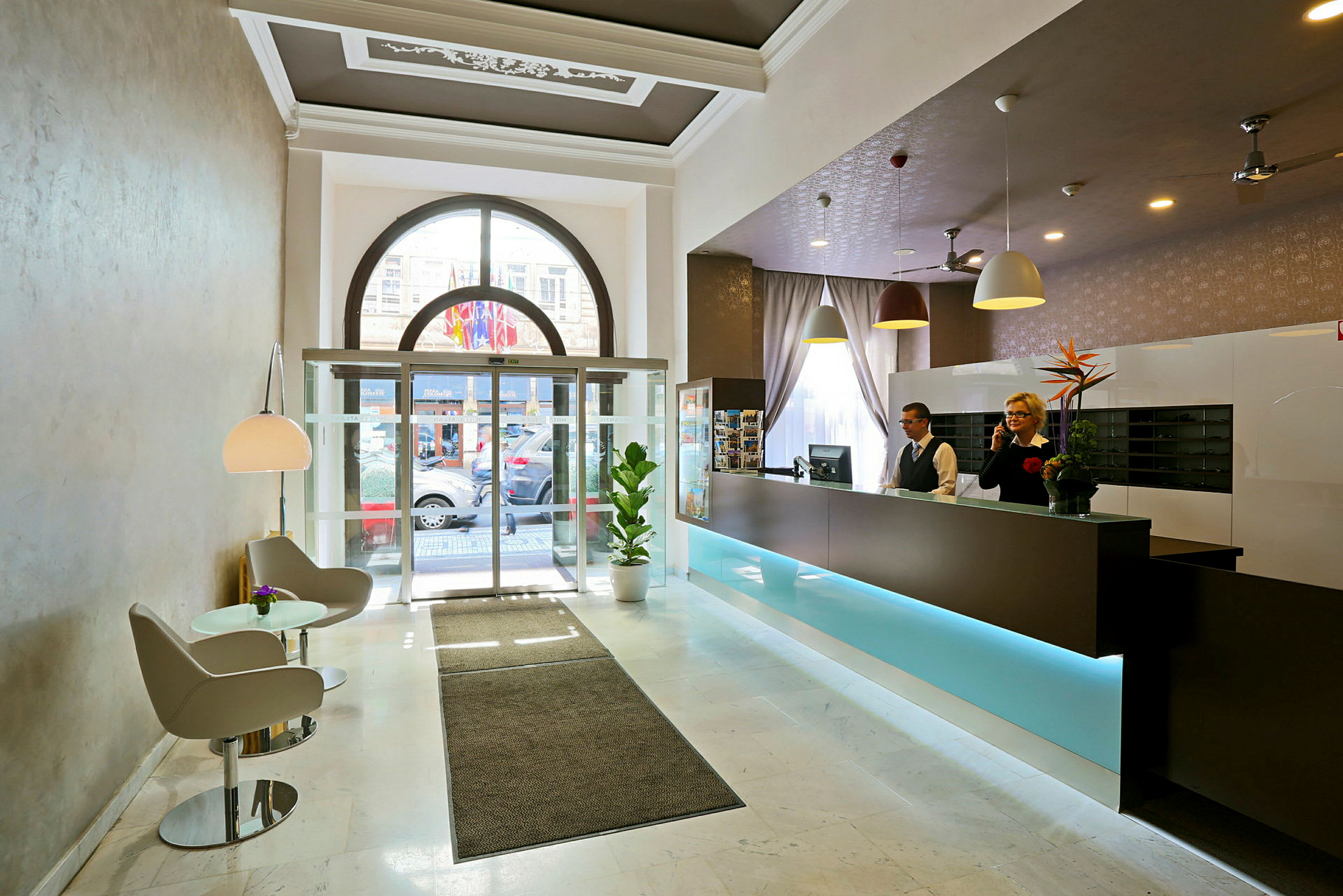 Hotellobby med reception, sittgrupp och glasdörrar mot utsidan. (AI-genererad text)