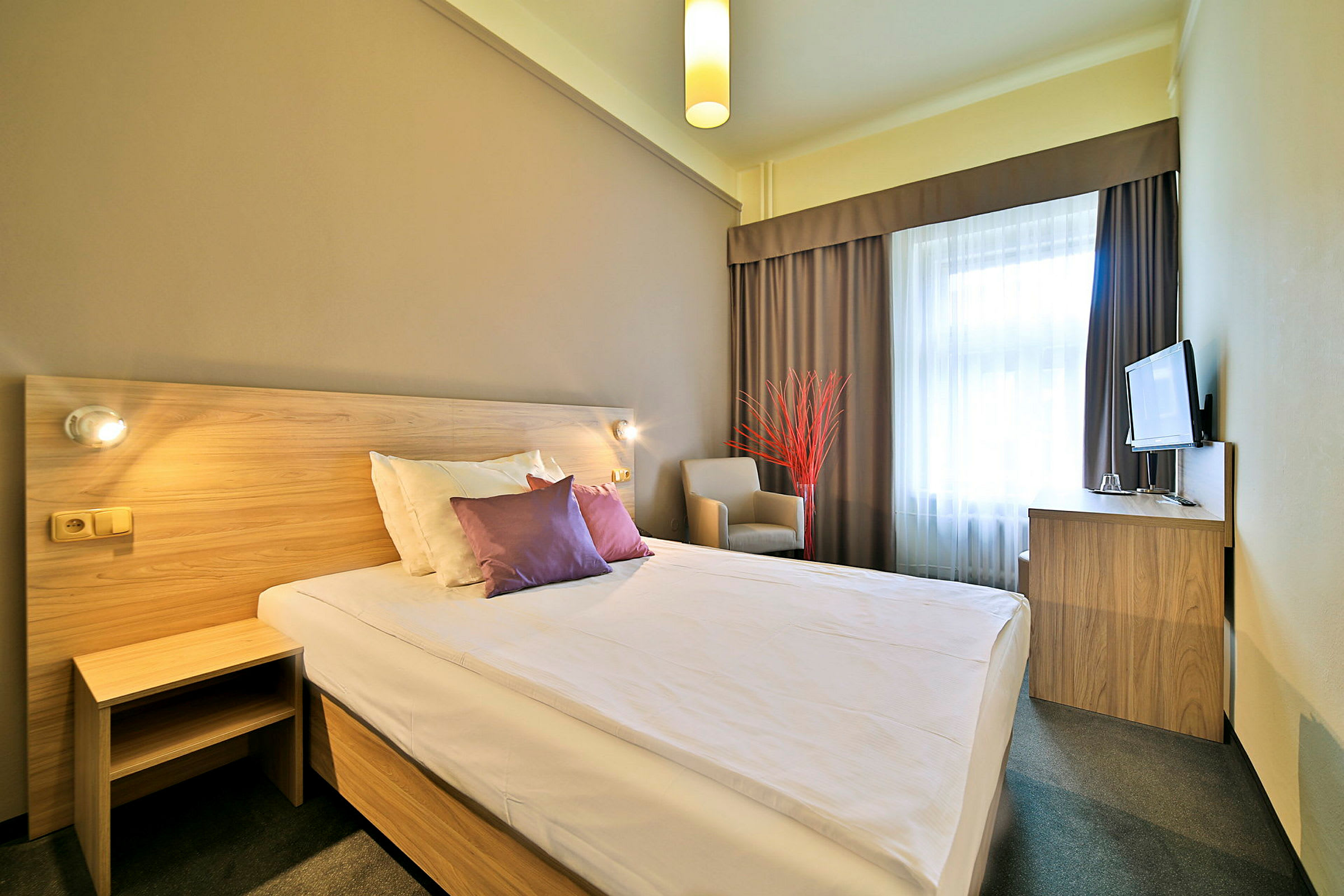 Ett hotellrum med en dubbelsäng, en stol, ett skrivbord med en TV och ett fönster med gardiner. (AI-genererad text)