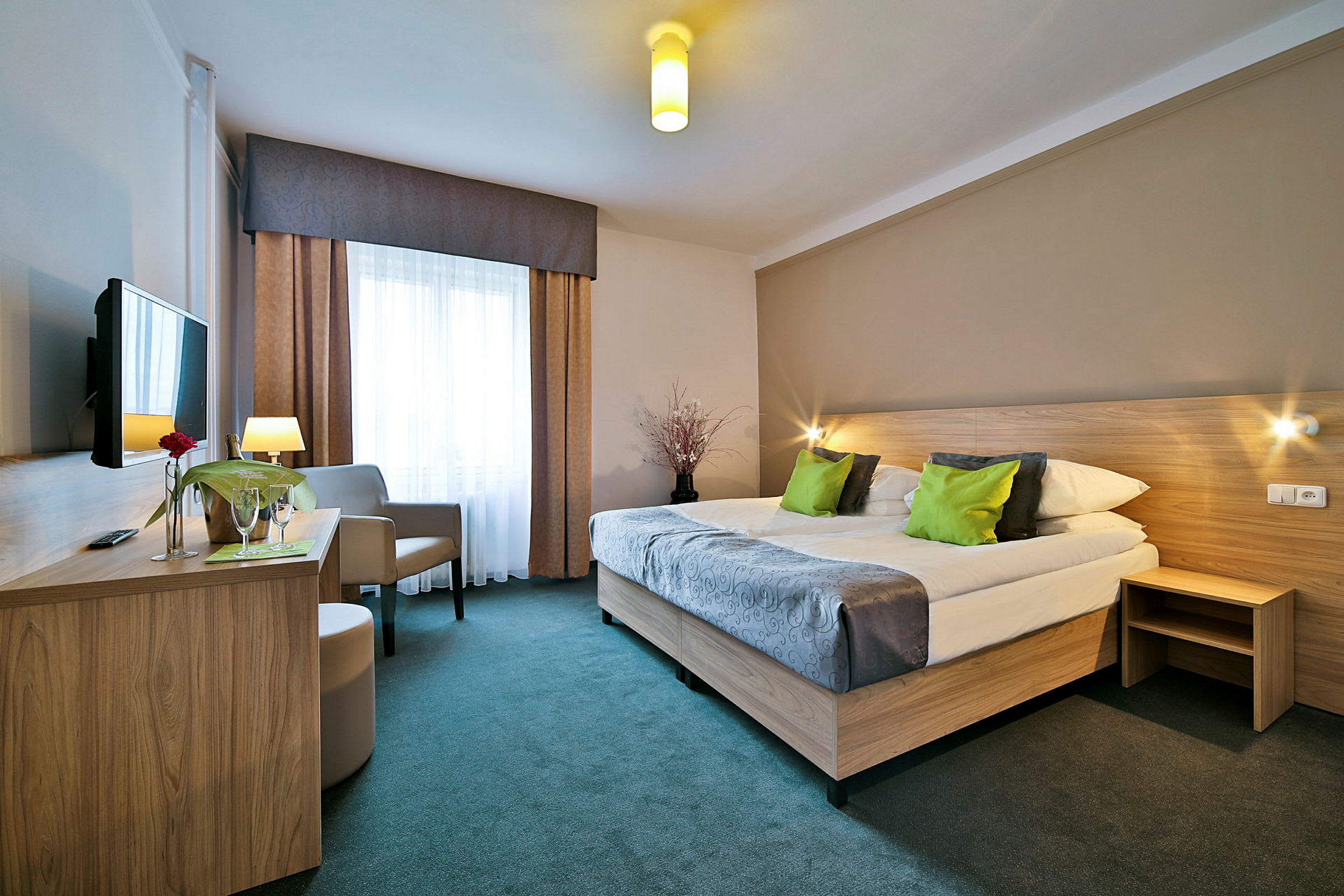 Hotellrum med dubbelsäng, gröna kuddar, skrivbord och TV. (AI-genererad text)