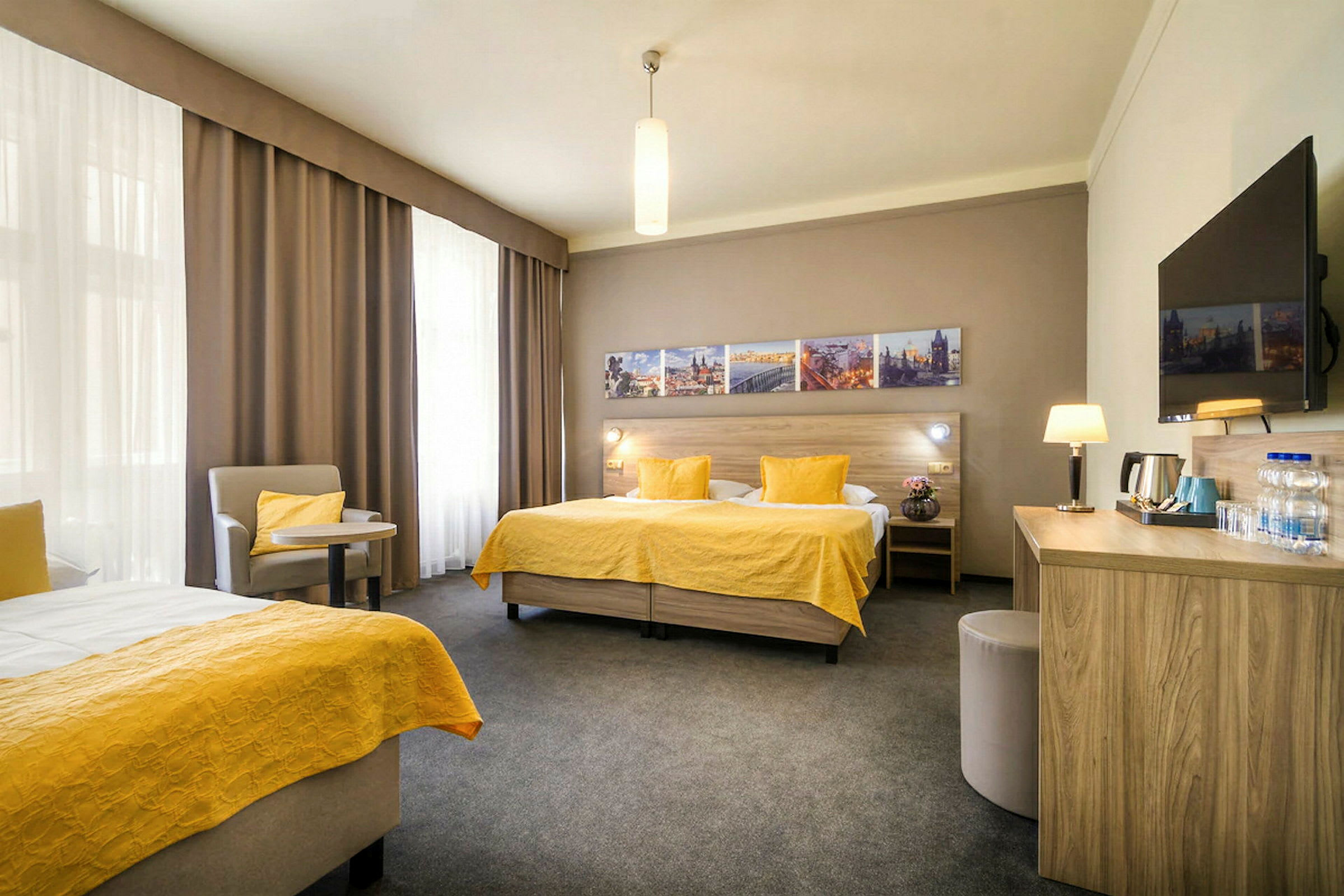 Ett hotellrum med två enkelsängar med gula överkast, en sittgrupp, ett skrivbord och en väggmonterad TV. (AI-genererad text)