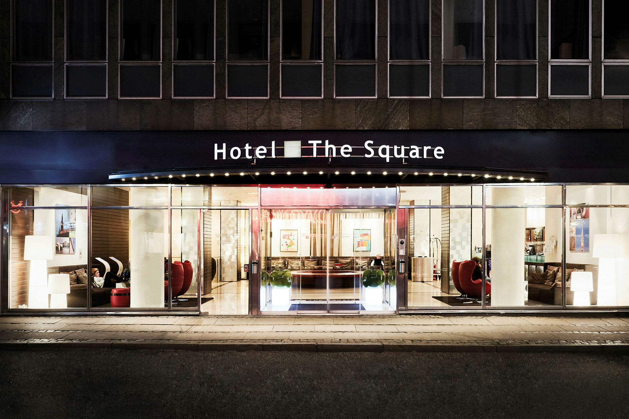 Entrén till ett hotell med namnet "The Square" belyst på kvällen. (AI-genererad text)