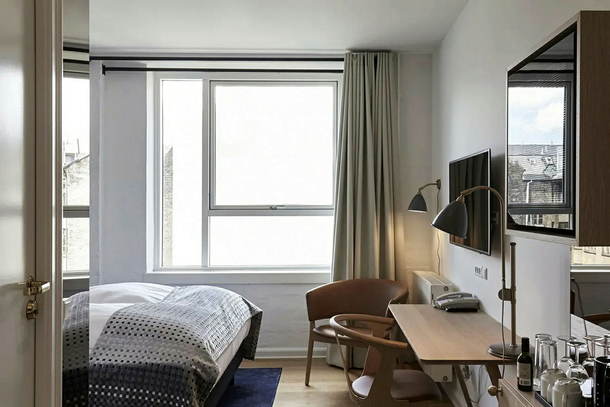 Bilden visar ett modernt hotellrum med en säng, ett skrivbord, en stol och ett stort fönster. (AI-genererad text)