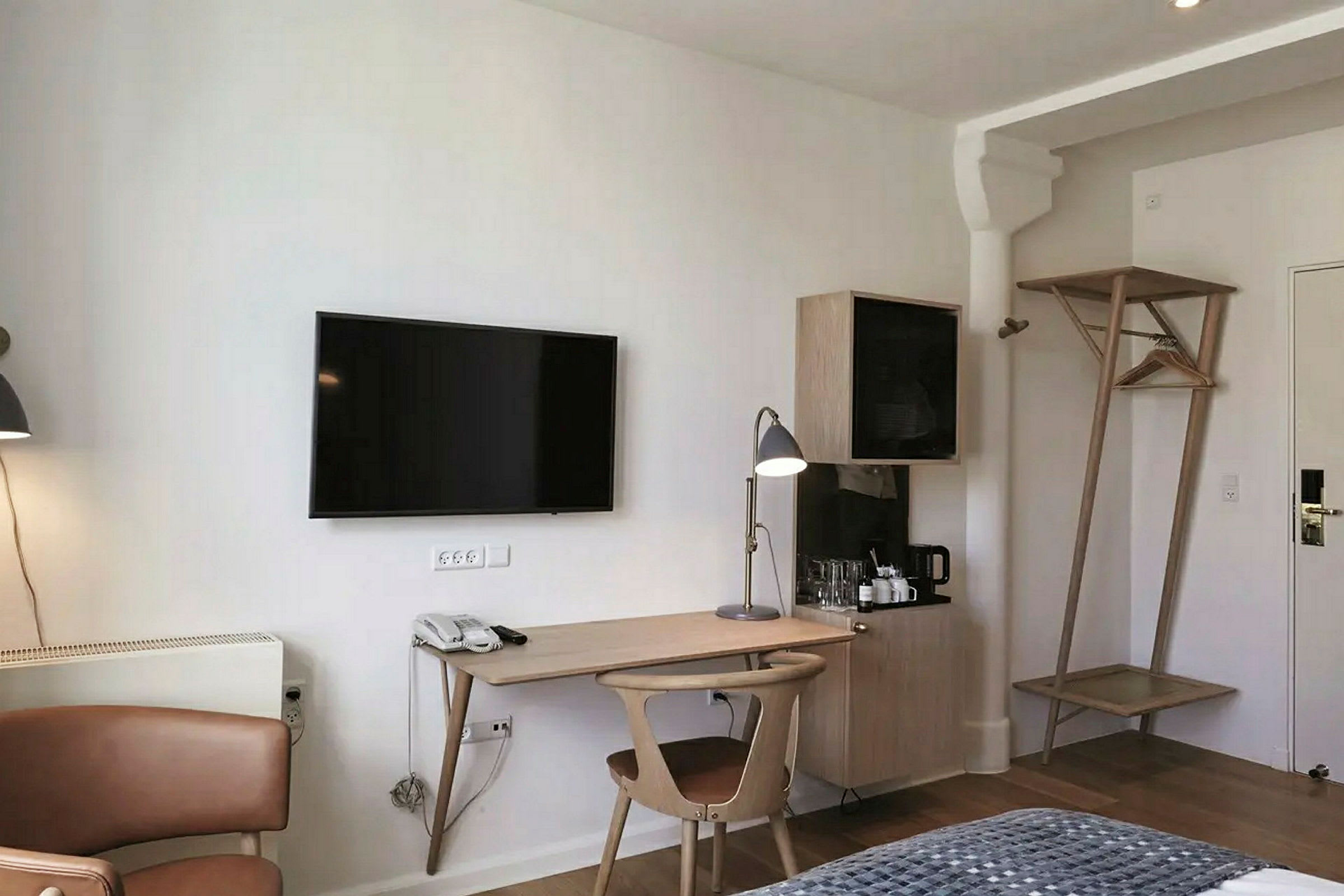 Ett hotellrum med en arbetsplats som inkluderar ett skrivbord, en stol och en skrivbordslampa. En TV är monterad på väggen ovanför. (AI-genererad text)