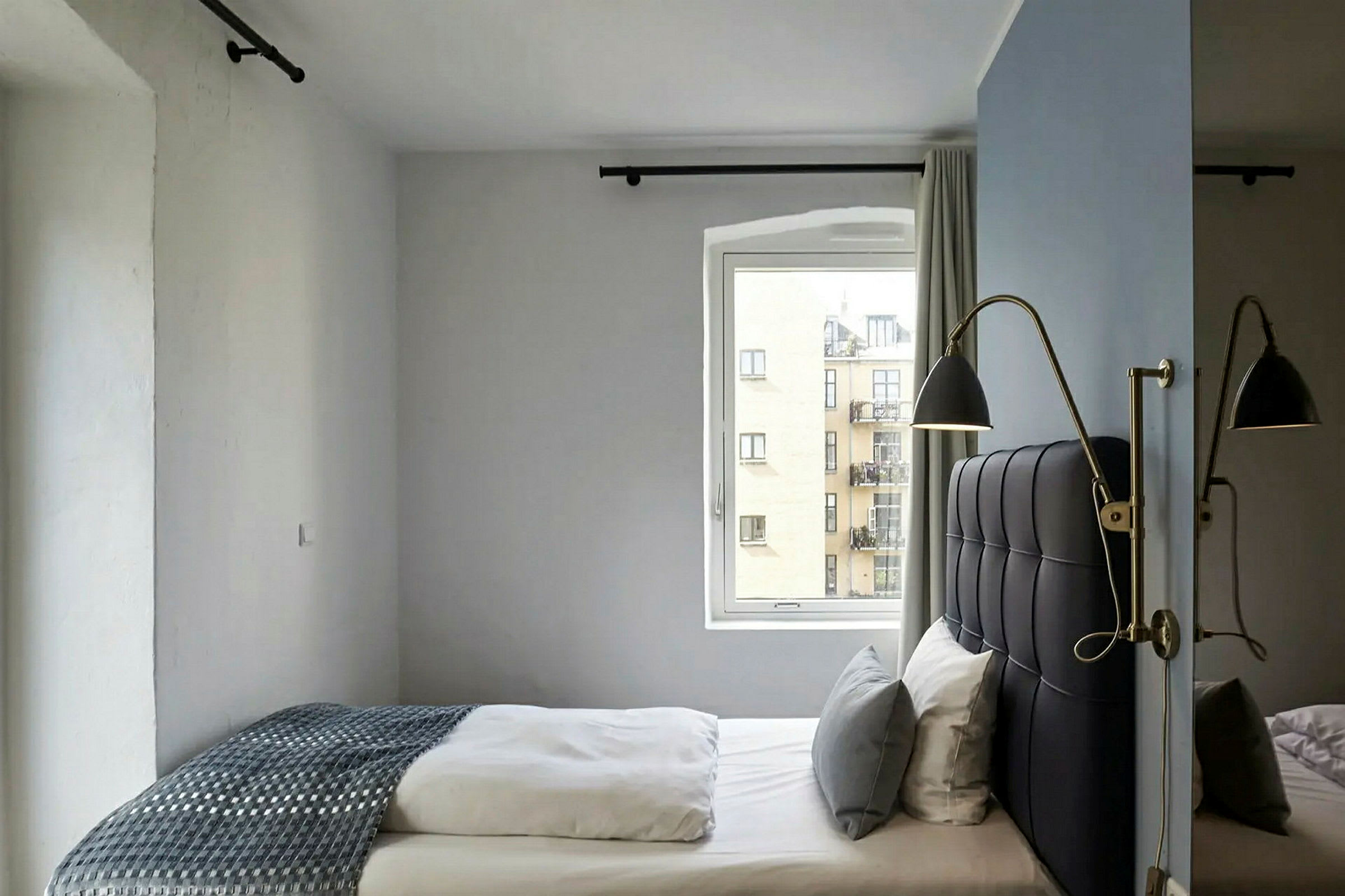 Ett hotellrum med en säng placerad nära ett fönster och vägglampor monterade vid sänggaveln. (AI-genererad text)