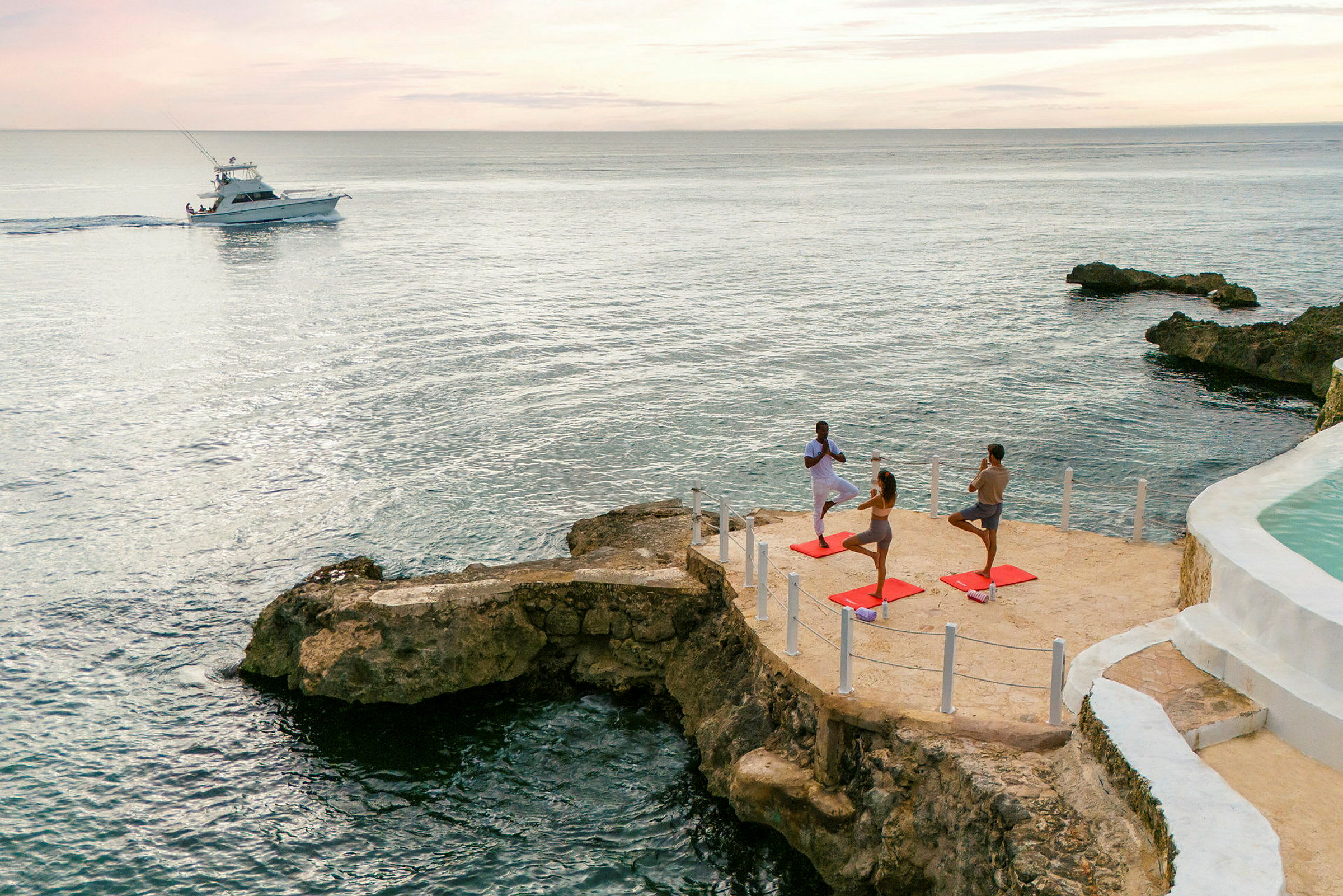 Personer som utövar yoga vid havet på en stenig klippa, med en båt på vattnet i bakgrunden. (AI-genererad text)