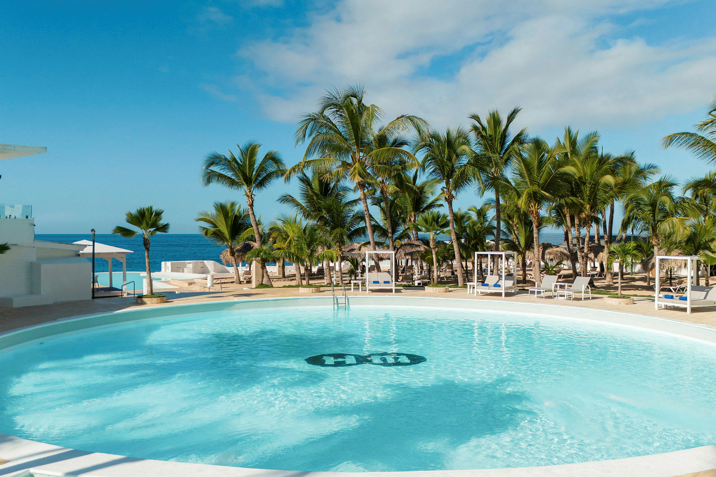 Bild av en pool omgiven av solsängar och palmer, med havet i bakgrunden. (AI-genererad text)