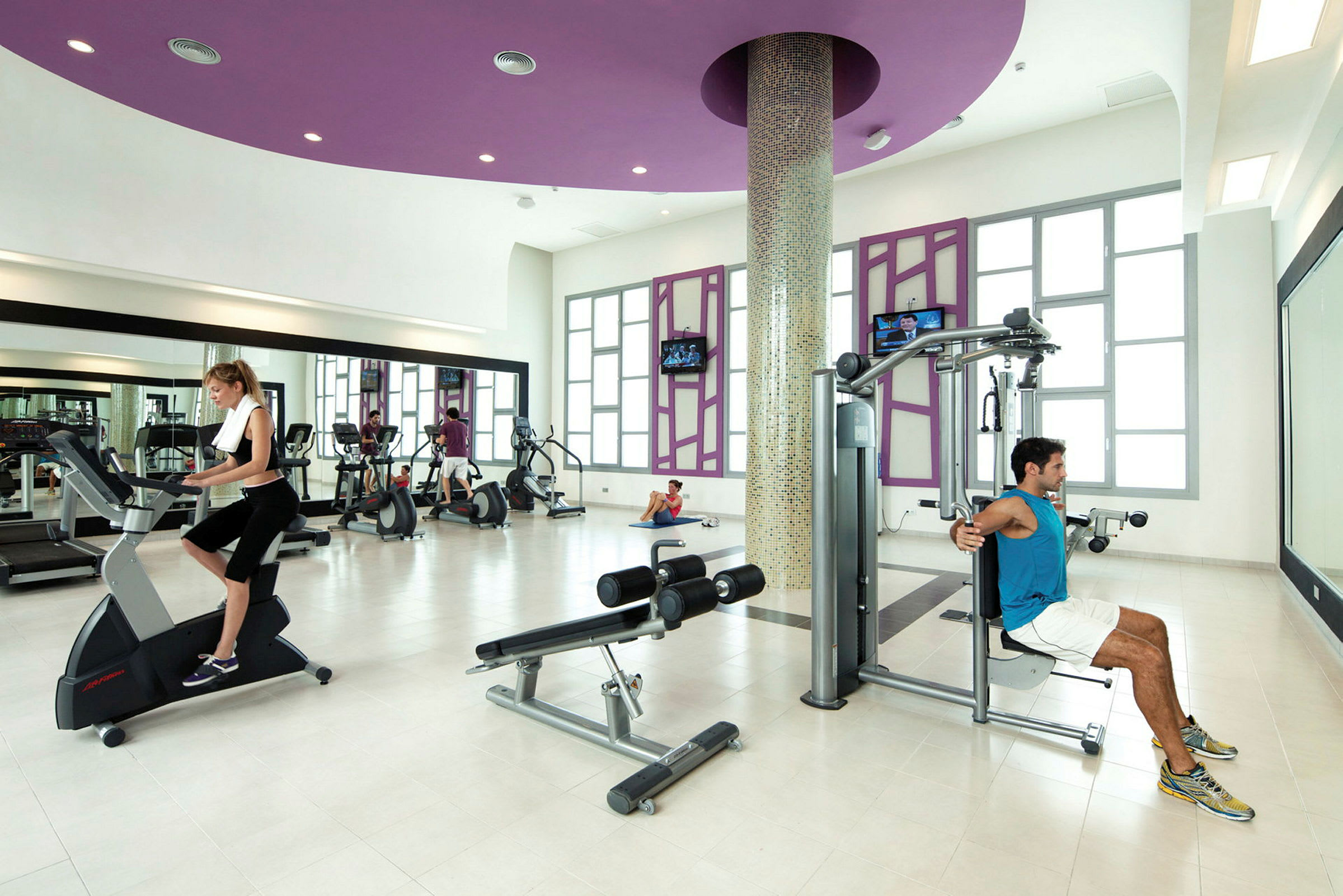 Ett gym med träningsmaskiner och personer som tränar. (AI-genererad text)